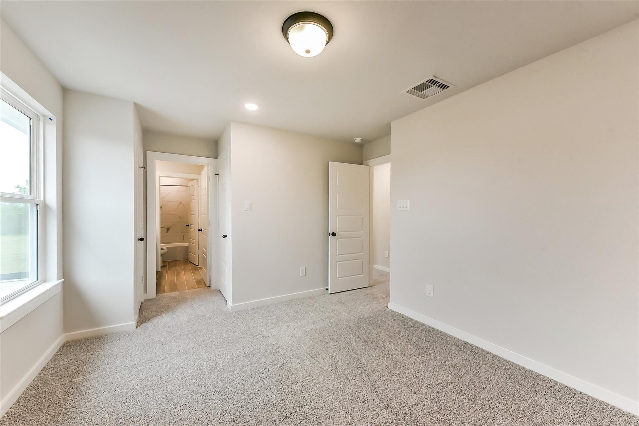 Bright bedroom with gray carpet, en-suite bath visible, large window, white walls in Davidson Homes Sequoia C, Crosby Texas