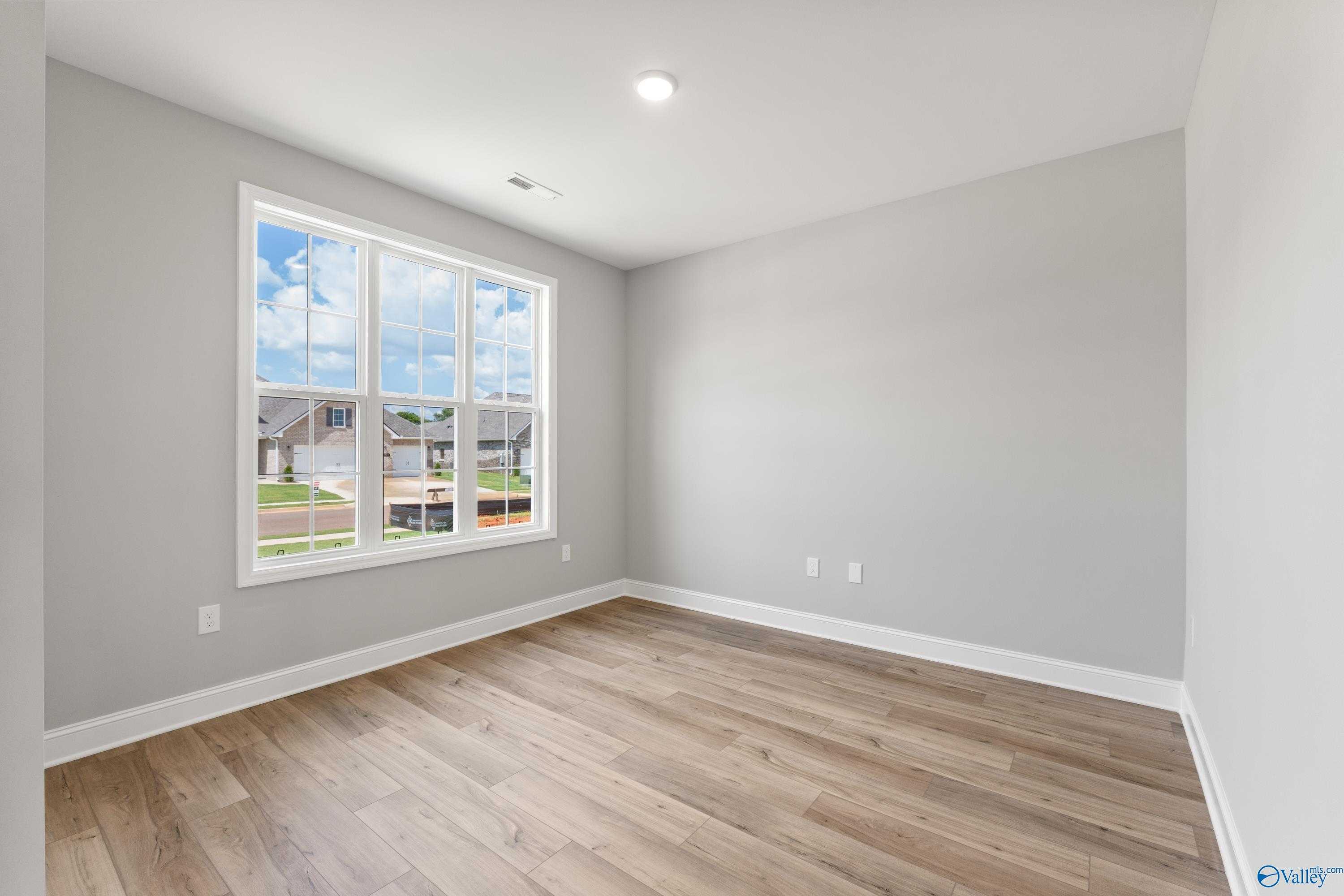 Bright secondary bedroom with gray walls, hardwood floors, and large window overlooking neighborhood in Davidson Homes The Rockford B, Toney, Alabama