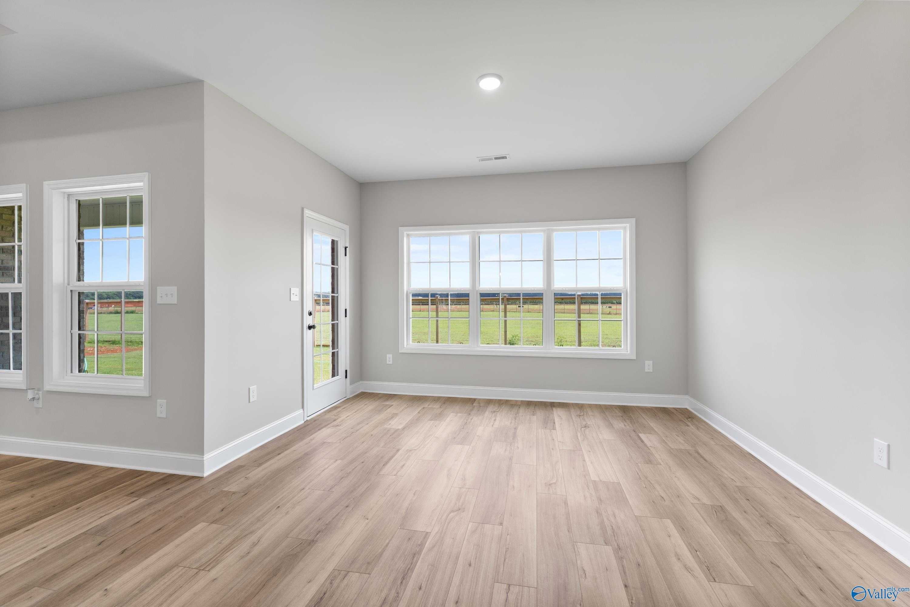 Bright sunroom with large windows overlooking green fields, gray walls, hardwood floors in The Finleigh home, Toney, Alabama