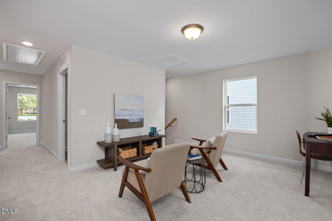 Upstairs loft with beige armchairs, wooden console table, desk, and large windows in Davidson Homes The Preston A, Lillington, NC