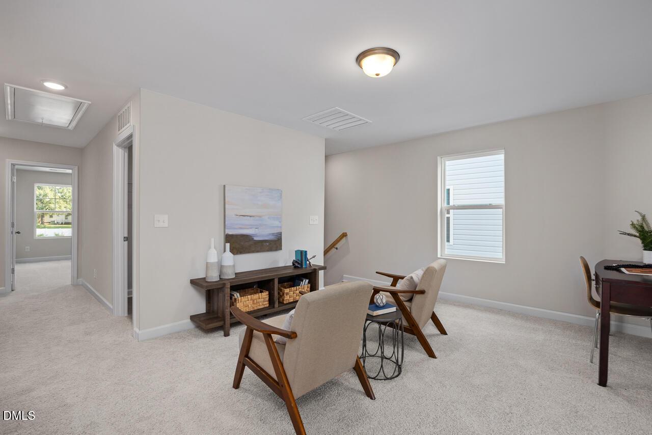 Upstairs loft with beige armchairs, wooden console table, desk, and large windows in Davidson Homes The Preston A, Lillington, NC