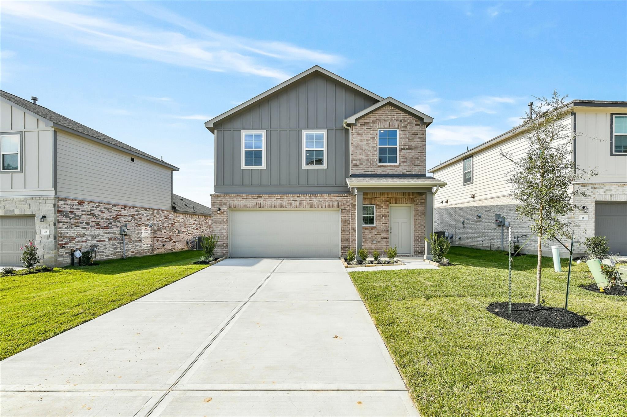 Modern 2-story gray brick home with 2-car garage, front porch, and lush lawn in Lakes at Black Oak, Magnolia, Texas