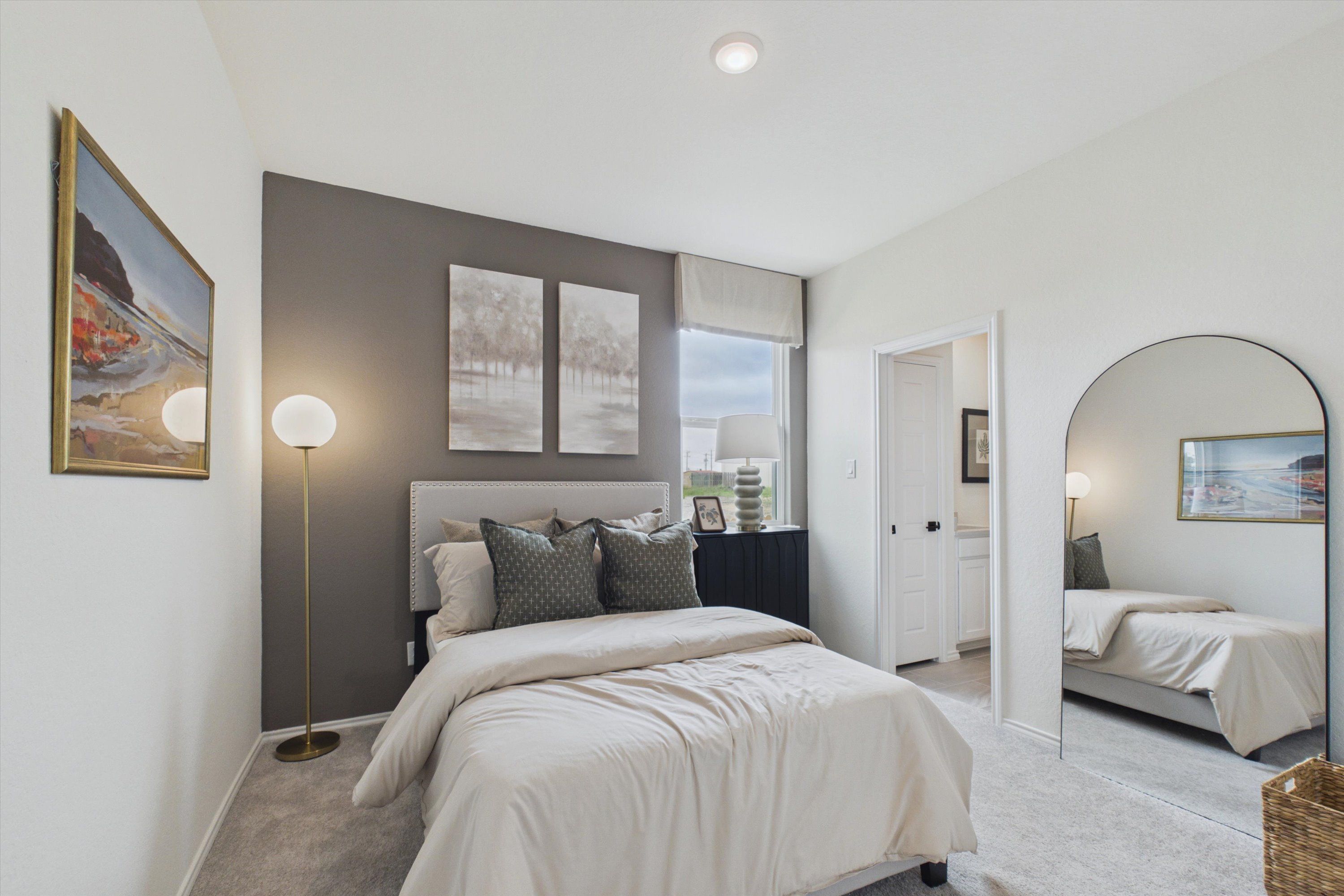 Cozy bedroom at Rayburn Valley in San Antonio TX by Davidson Homes with gray accent wall, plush white bed, abstract art, and arched mirror