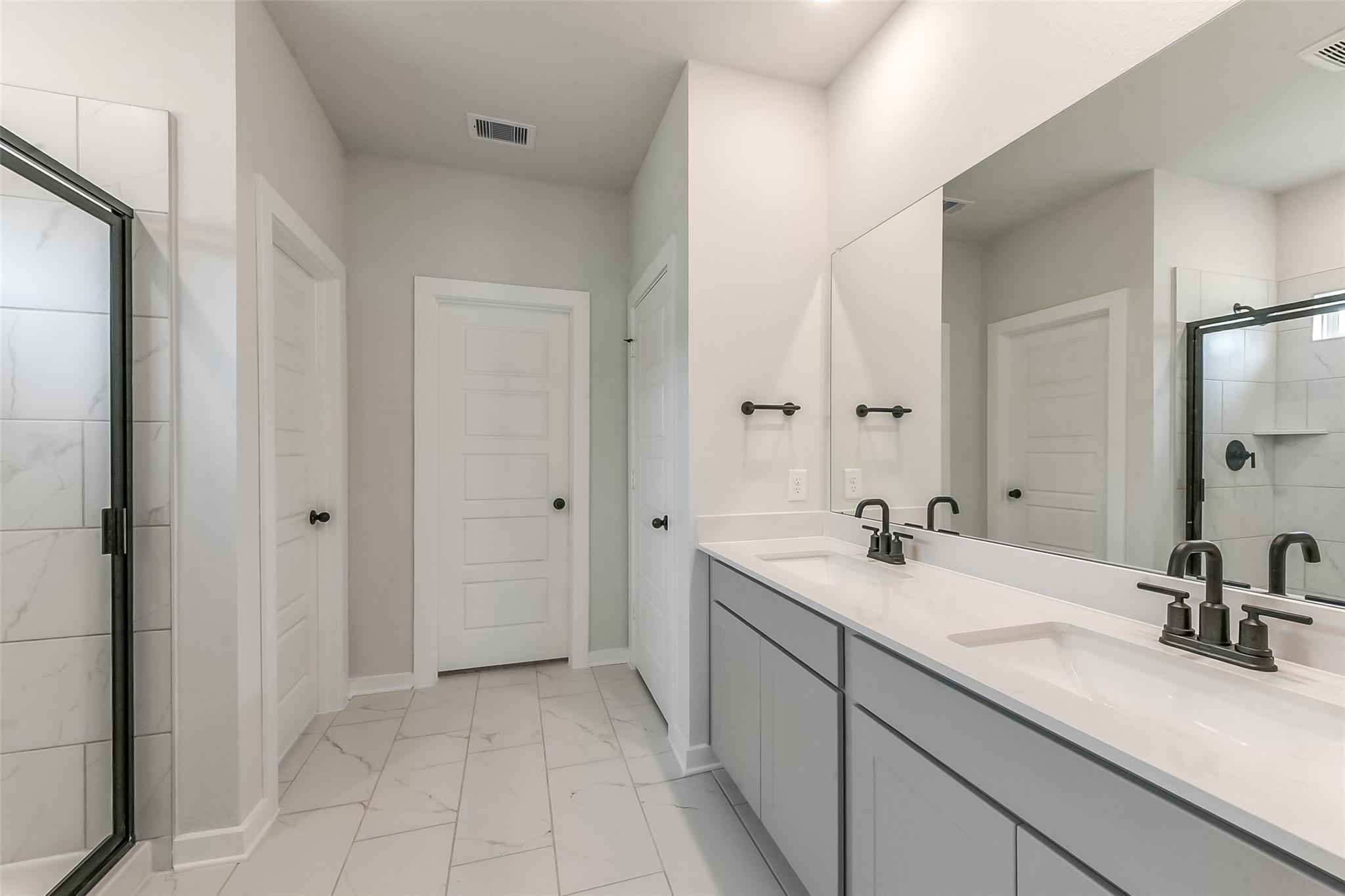 Modern master bathroom featuring double vanity with quartz counters, gray cabinets, frameless glass shower in Davidson Homes The Everett C, Crosby, Texas