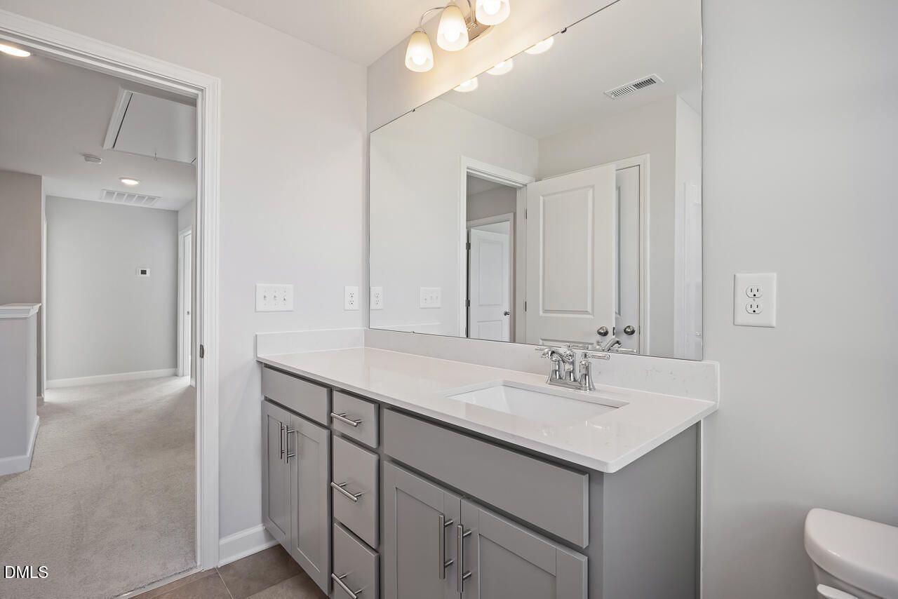 Modern double vanity bathroom with quartz countertop, gray cabinets, and large mirror in Davidson Homes The Willow G, Angier, NC