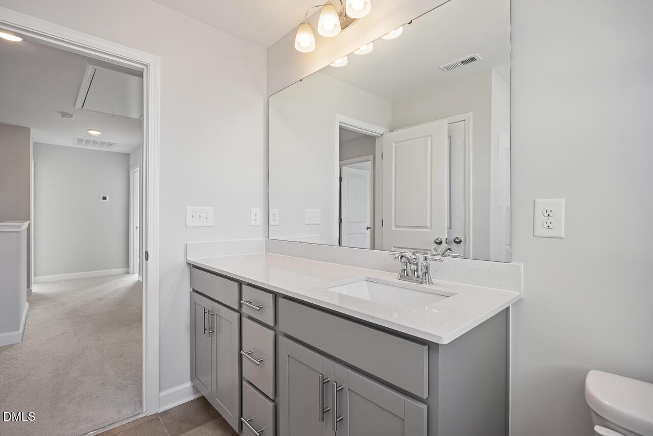 Modern double vanity bathroom with quartz countertop, gray cabinets, and large mirror in Davidson Homes The Willow G, Angier, NC