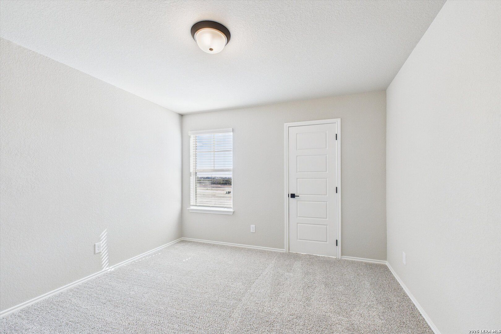 Bright secondary bedroom with light gray walls, large window, white door, and carpet floor in Davidson Homes The Charlotte A, San Antonio