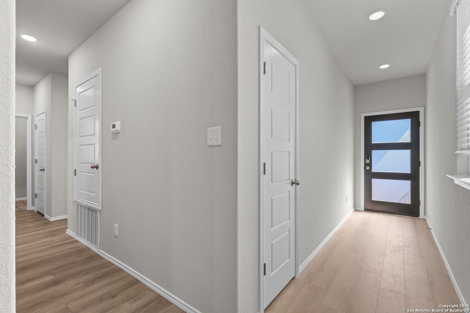Bright entry hallway with white doors, glass-panel front door, and wood floors in Davidson Homes The Colorado B, San Antonio