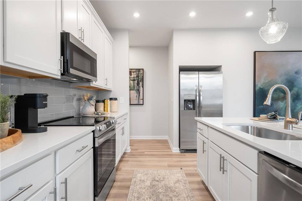 Modern white kitchen with stainless steel appliances, large island sink, and open hallway in Davidson Homes Wilmington B, Emerson, GA