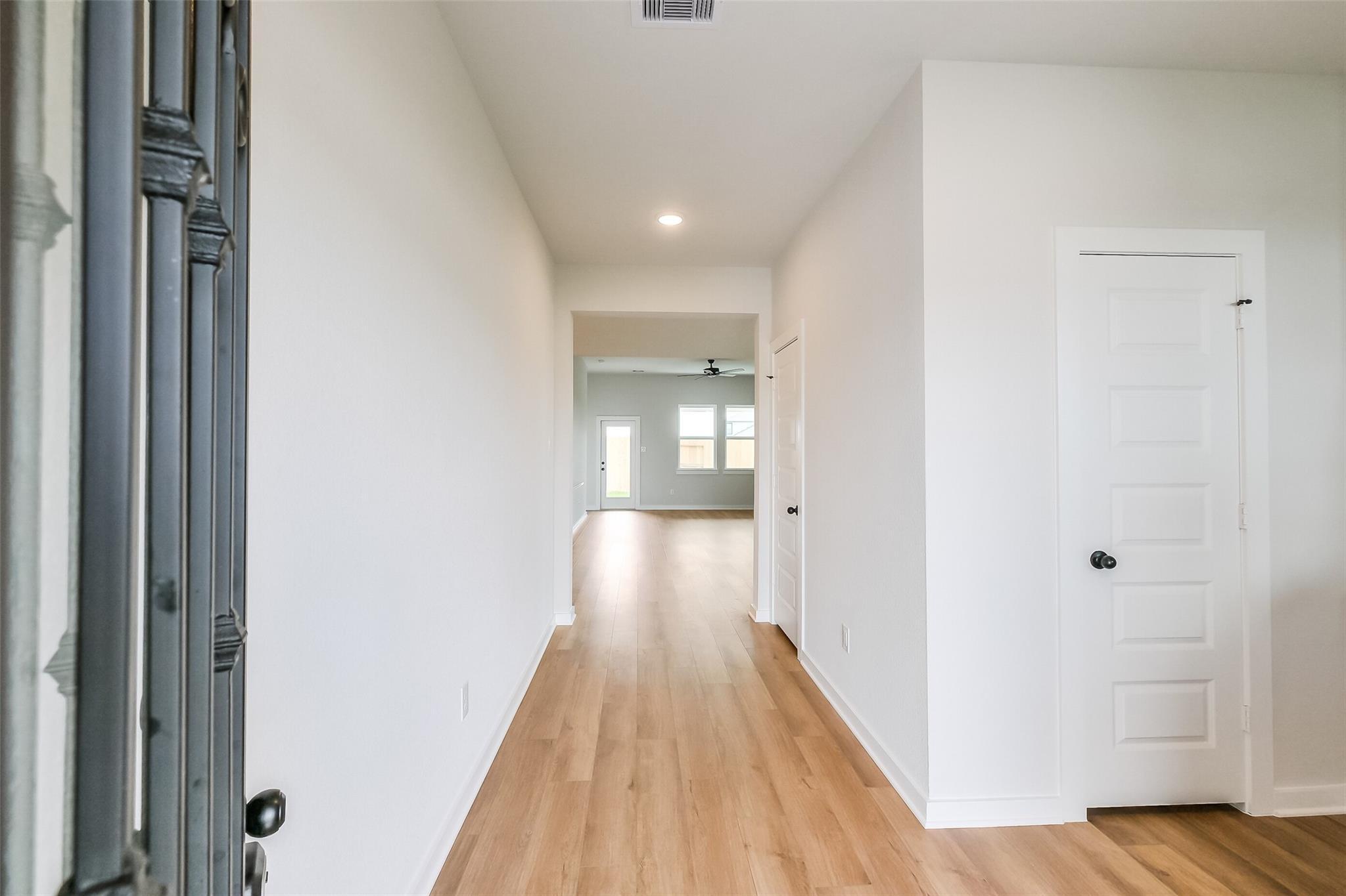 Elegant entry hallway with ornate metal door, light oak floors, and white walls in Davidson Homes The Tierra B, Beasley, Texas