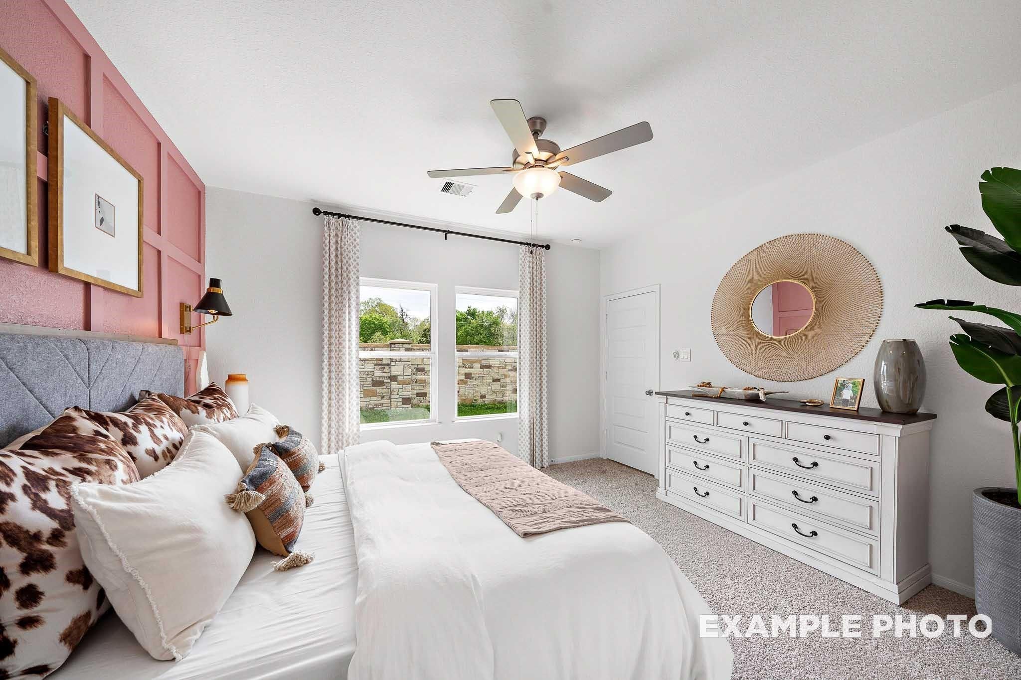 Cozy bedroom with pink accent wall, plush white bed, ceiling fan, and large windows in Davidson Homes The Sabine F, Magnolia, Texas