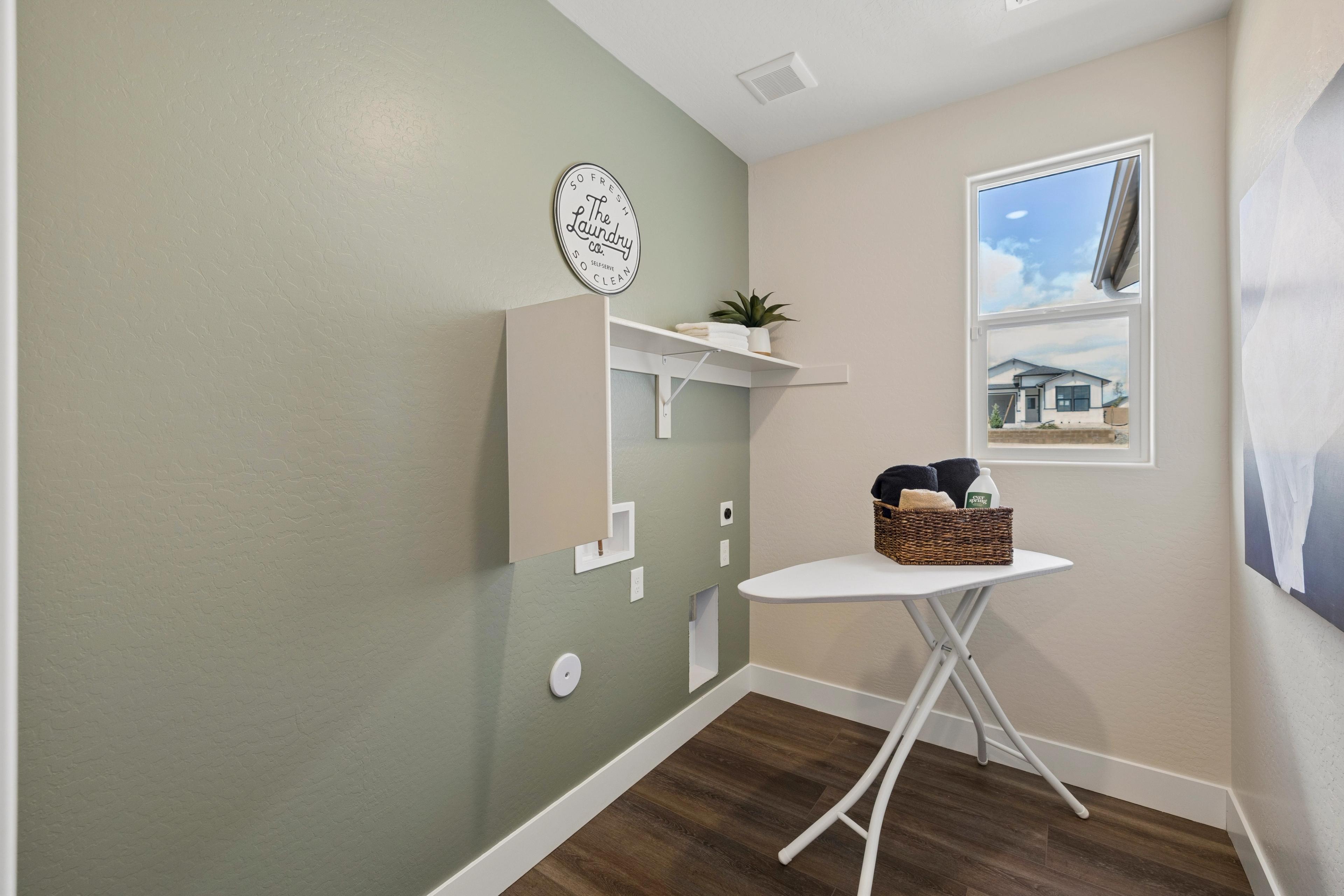 Modern laundry room in South Ranch Western Collection, Prescott AZ with sage walls, ironing board, towel basket, and utility hookups