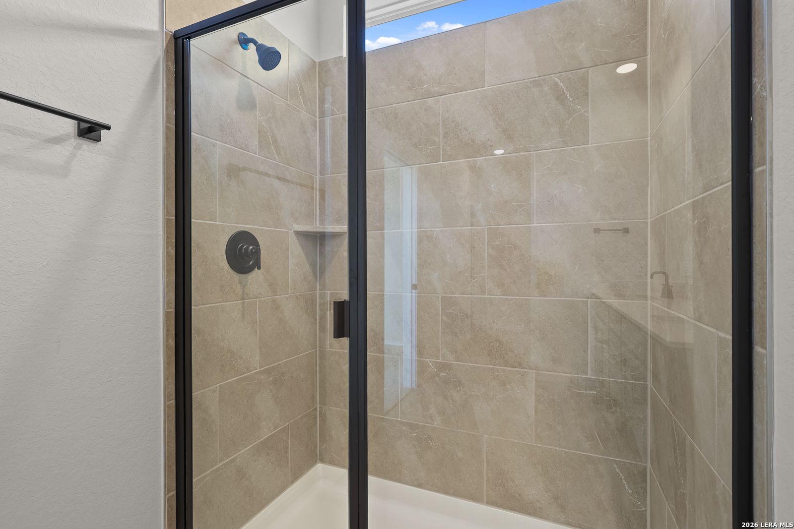 Frameless glass walk-in shower with beige tile and black fixtures in Davidson Homes Glenwood E bathroom, Comanche Ridge San Antonio
