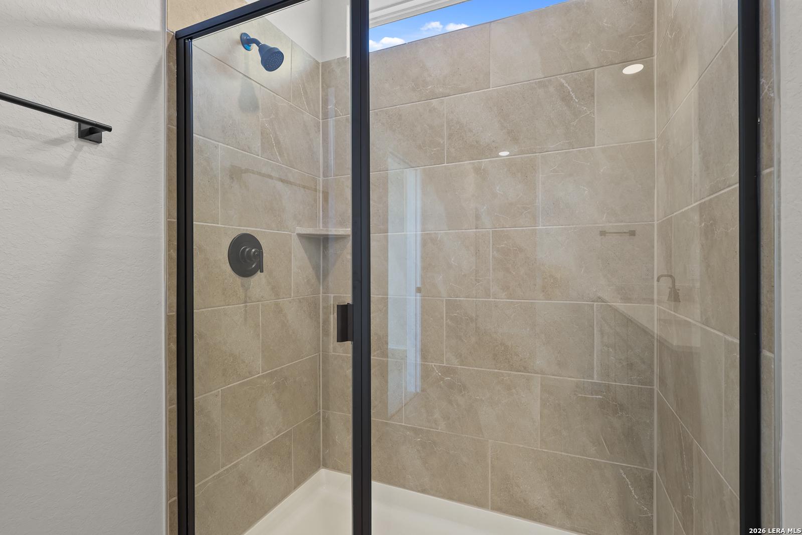Frameless glass walk-in shower with beige tile and black fixtures in Davidson Homes Glenwood E bathroom, Comanche Ridge San Antonio
