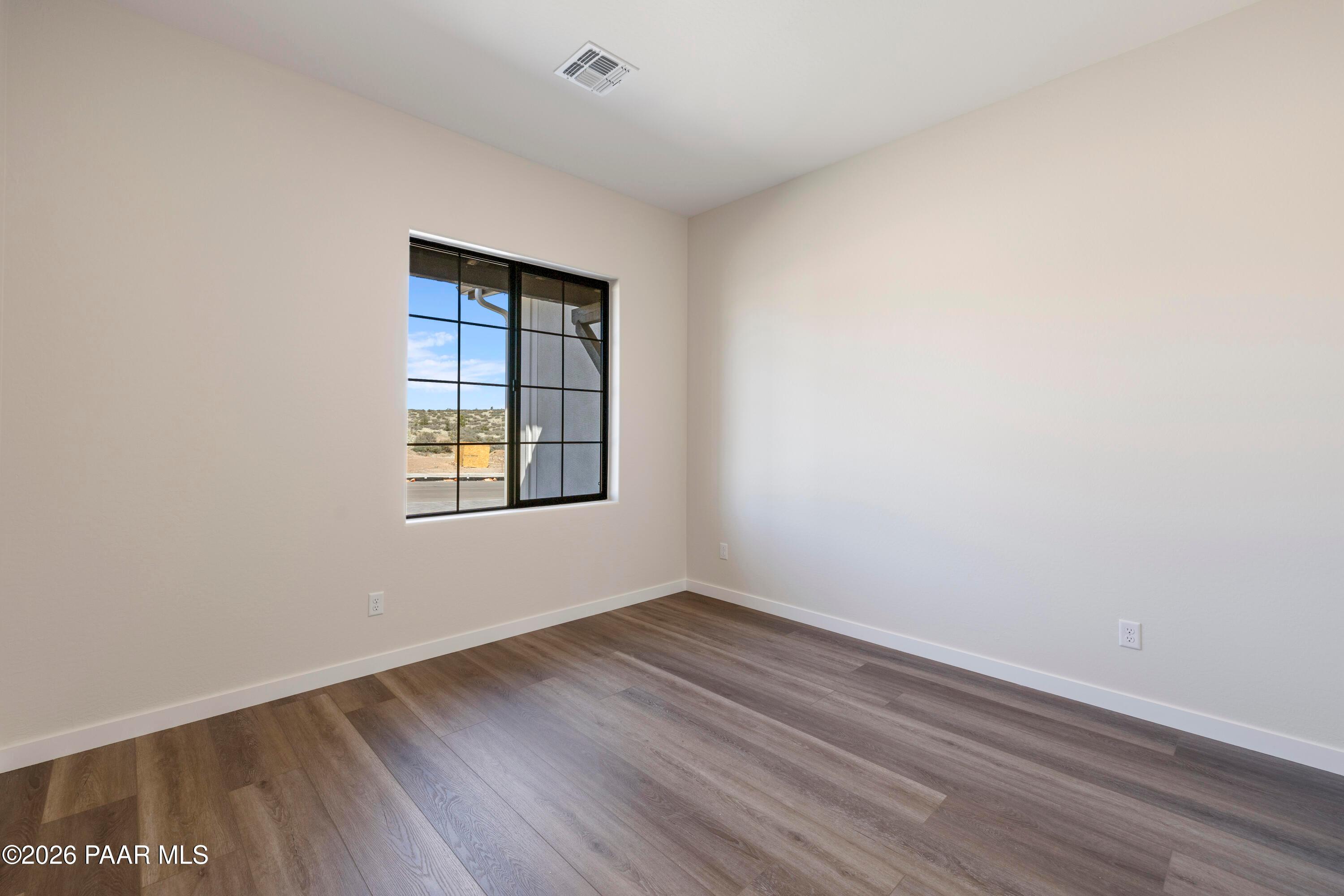 Bright bedroom with large black-framed window overlooking desert and hardwood floors in Davidson Homes The Soleil E, Prescott, AZ