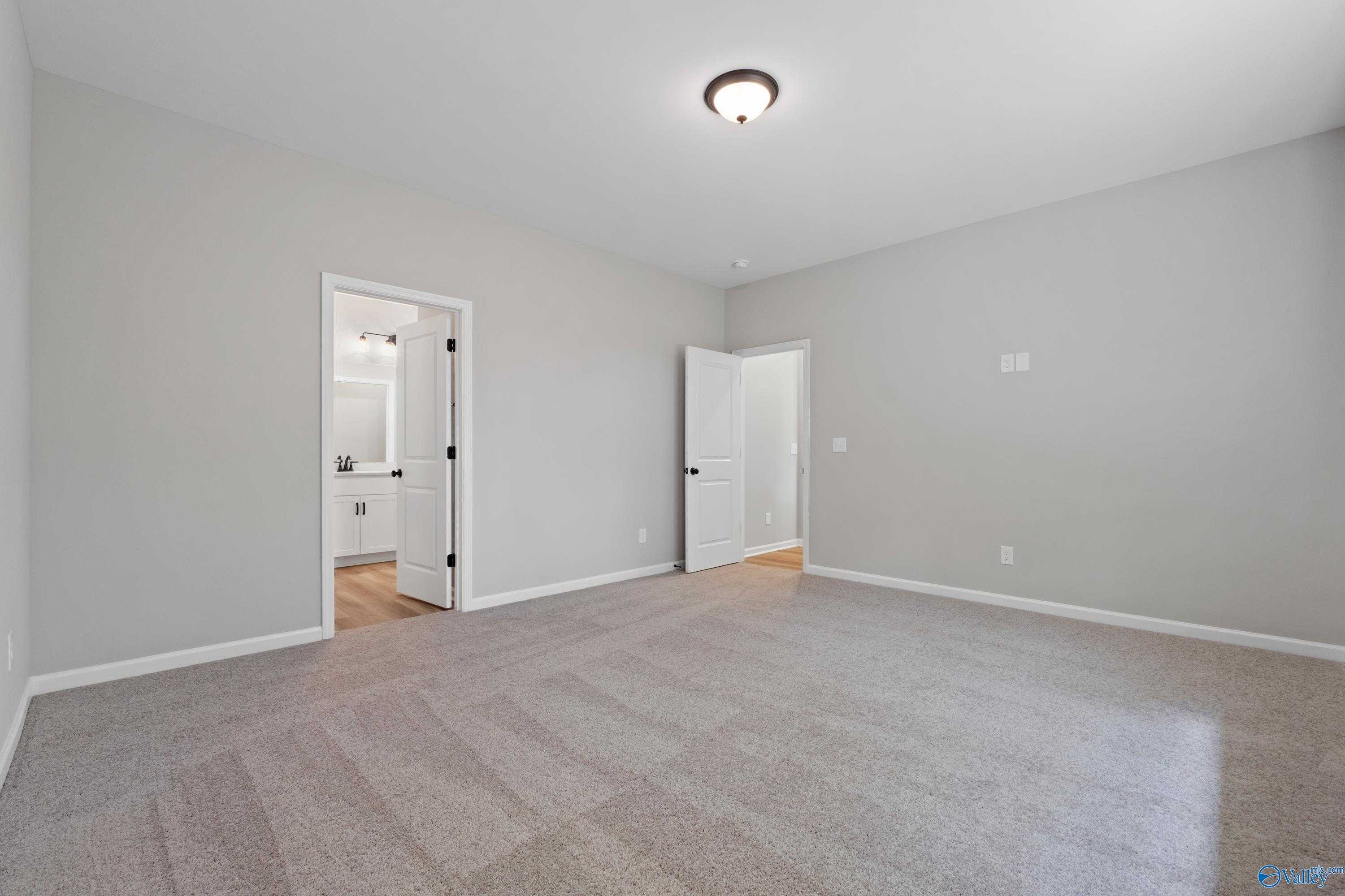Bright secondary bedroom with attached bath, neutral gray walls, and carpet in Evermore Homes The Nantucket, Madison, Alabama