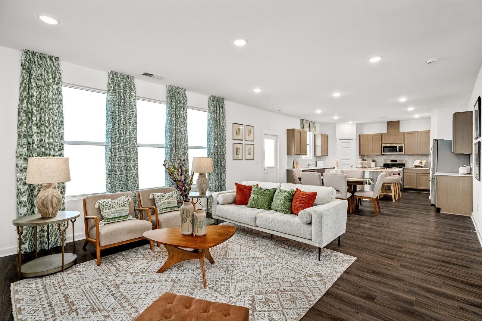 Open-concept living room with beige sofa, patterned rug, and armchairs adjacent to modern kitchen with white cabinets in Davidson Homes The Gordon C, White House, TN
