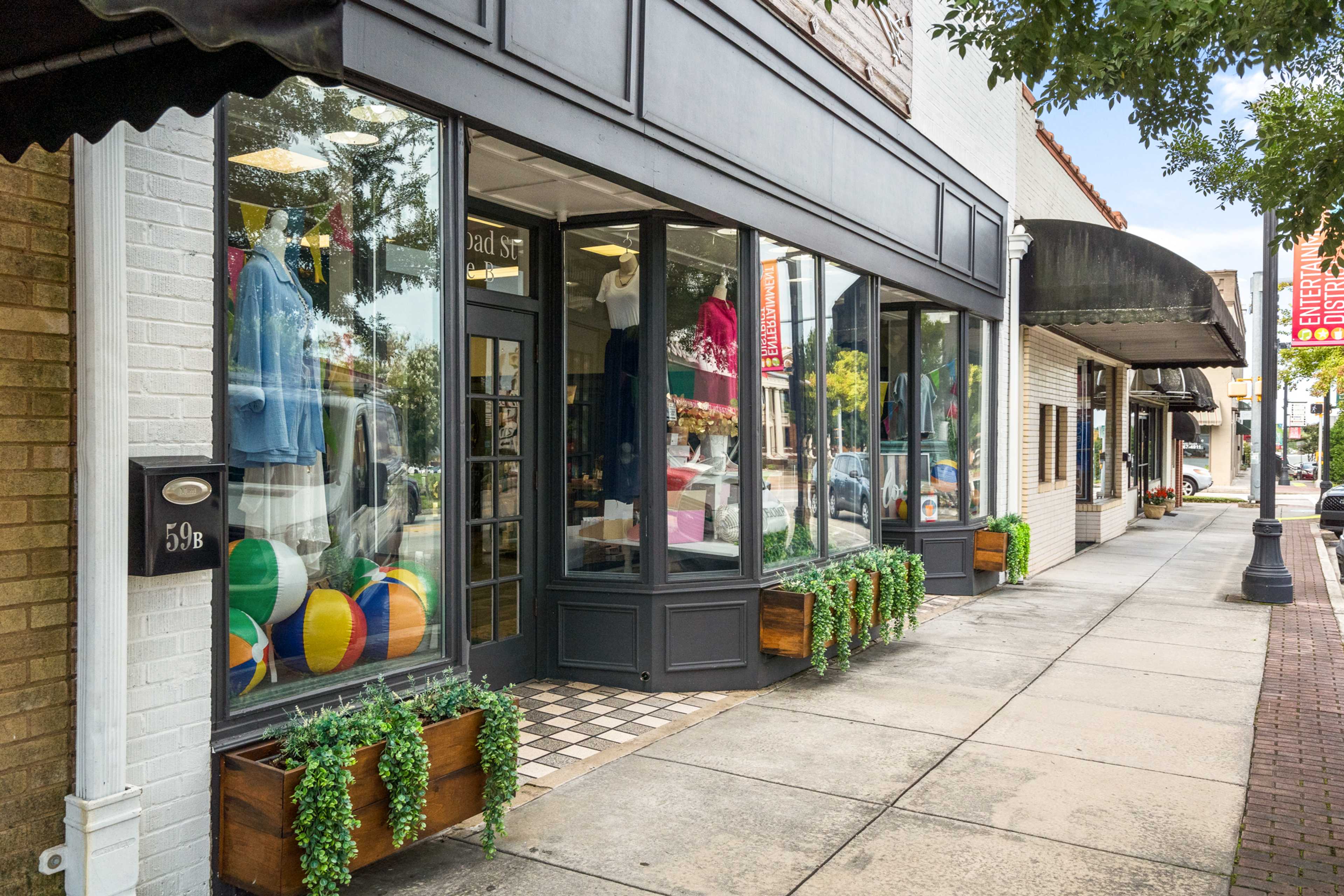Charming brick boutique in Winder Georgia with colorful apparel displays, beach balls, awnings, potted plants, and tree-lined sidewalk