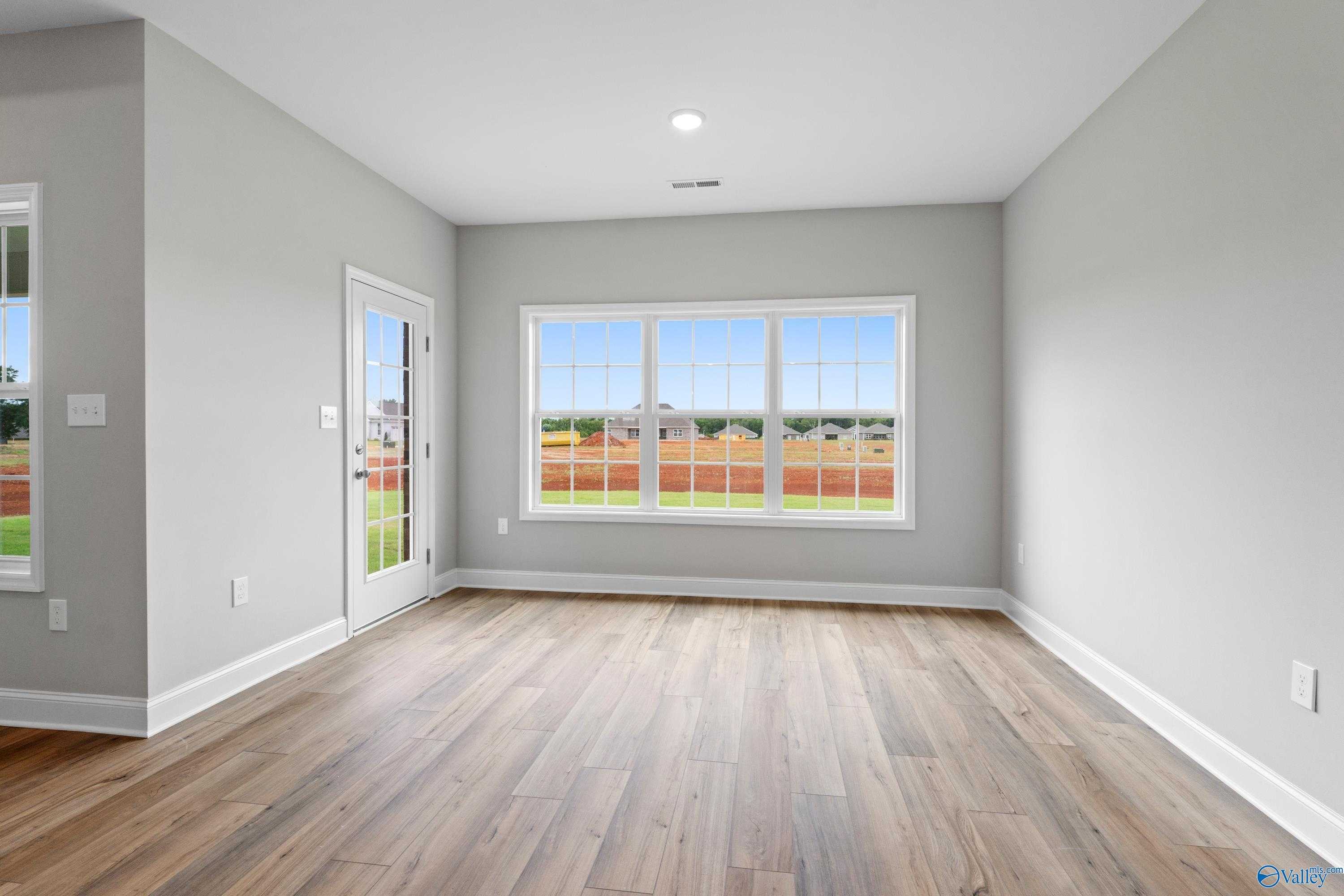 Bright living room with gray walls, hardwood floors, large windows, and French doors overlooking green field in The Finleigh, Meridianville, Alabama