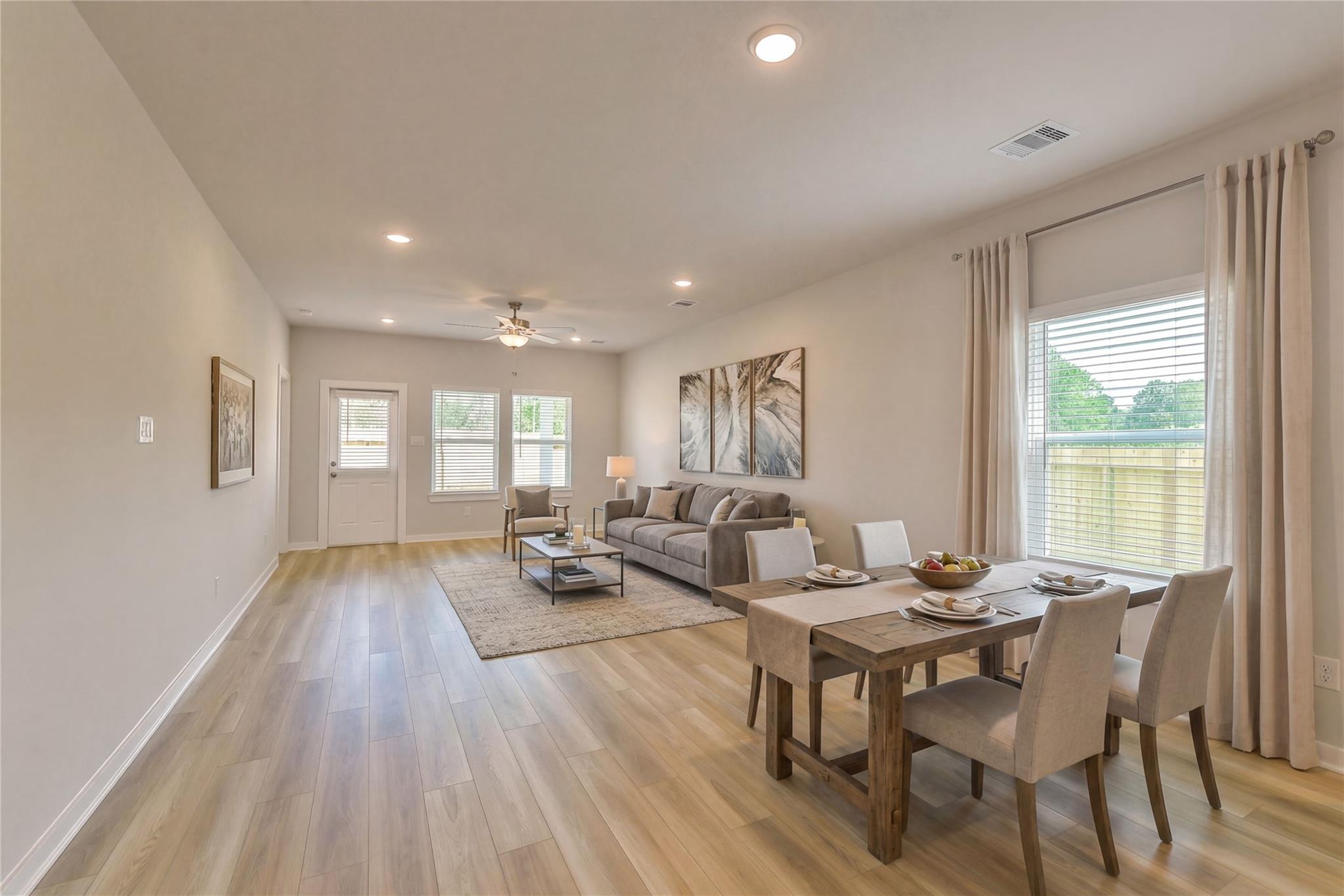 Open living-dining area with gray sectional sofa, rustic wood table set for dining, luxury vinyl plank floors in Davidson Homes San Marcos E, Conroe TX