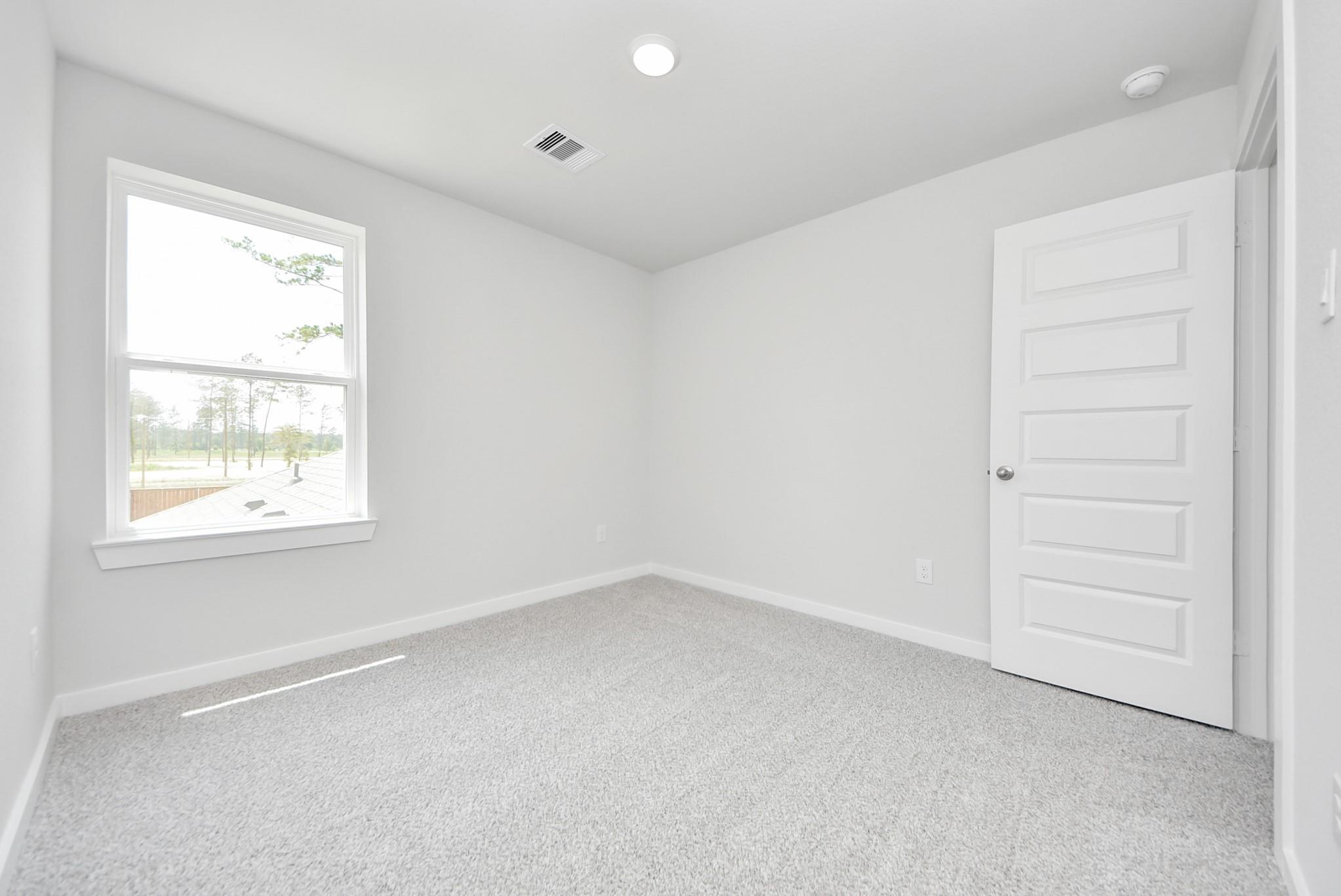 Bright, carpeted bedroom with white walls and natural light in The Blanco F floor plan at Spring Branch Crossing, Conroe.