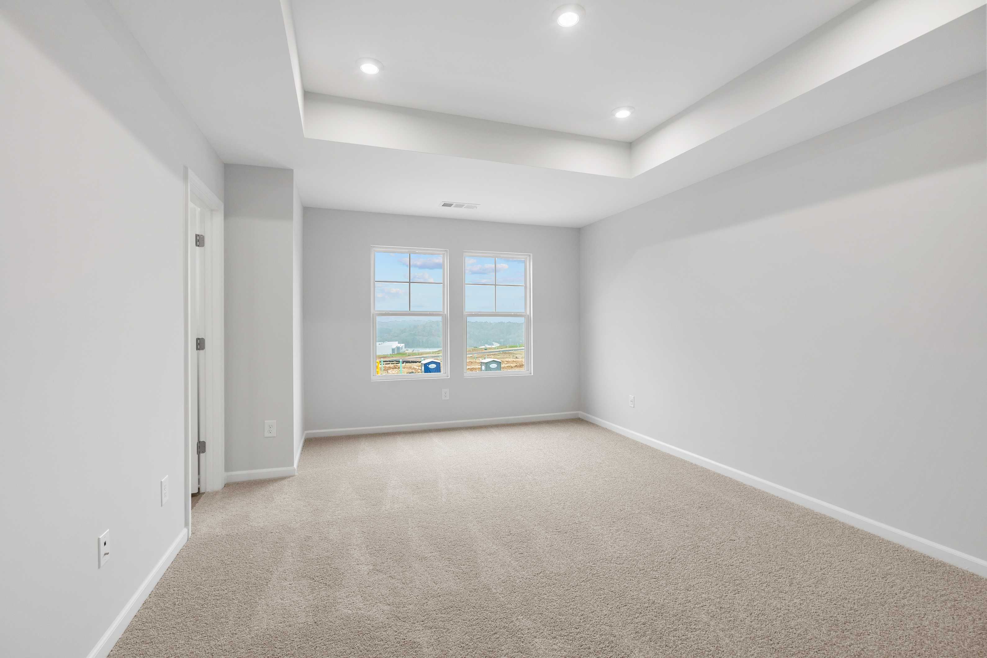 Spacious upstairs master bedroom in The Durant A featuring gray walls, beige carpet, large windows, and tray ceiling