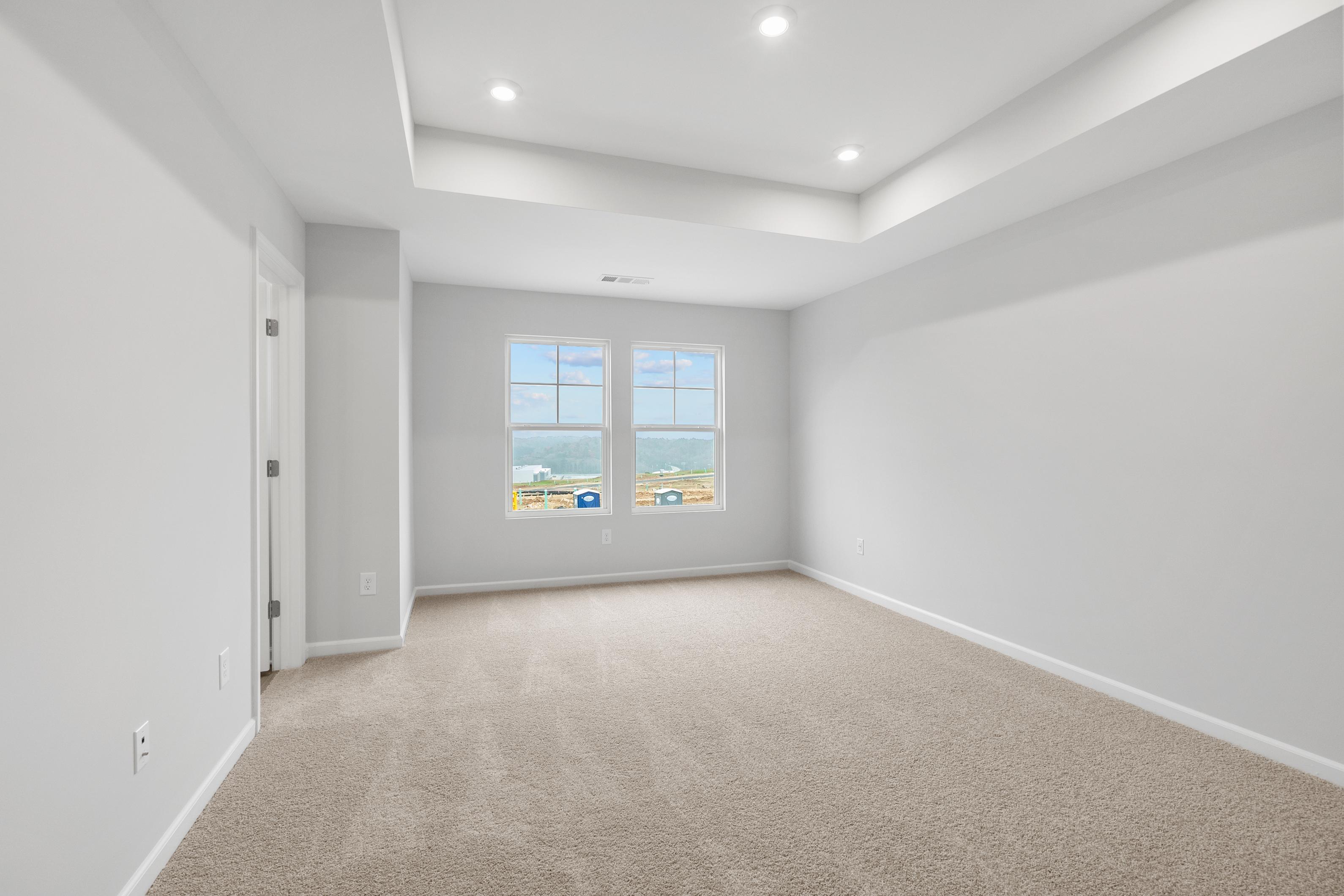 Spacious upstairs master bedroom in The Durant A featuring gray walls, beige carpet, large windows, and tray ceiling