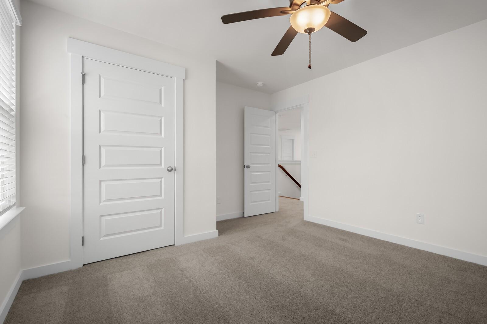 Bright, carpeted bedroom with ceiling fan in The Ash A floor plan at Woods Crossing, Gallatin, Tennessee.