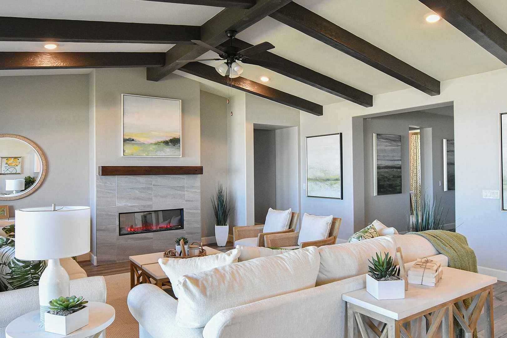 Spacious living room in The Summit B featuring white sectional sofa, stone gas fireplace, abstract wall art, and wooden beam ceiling