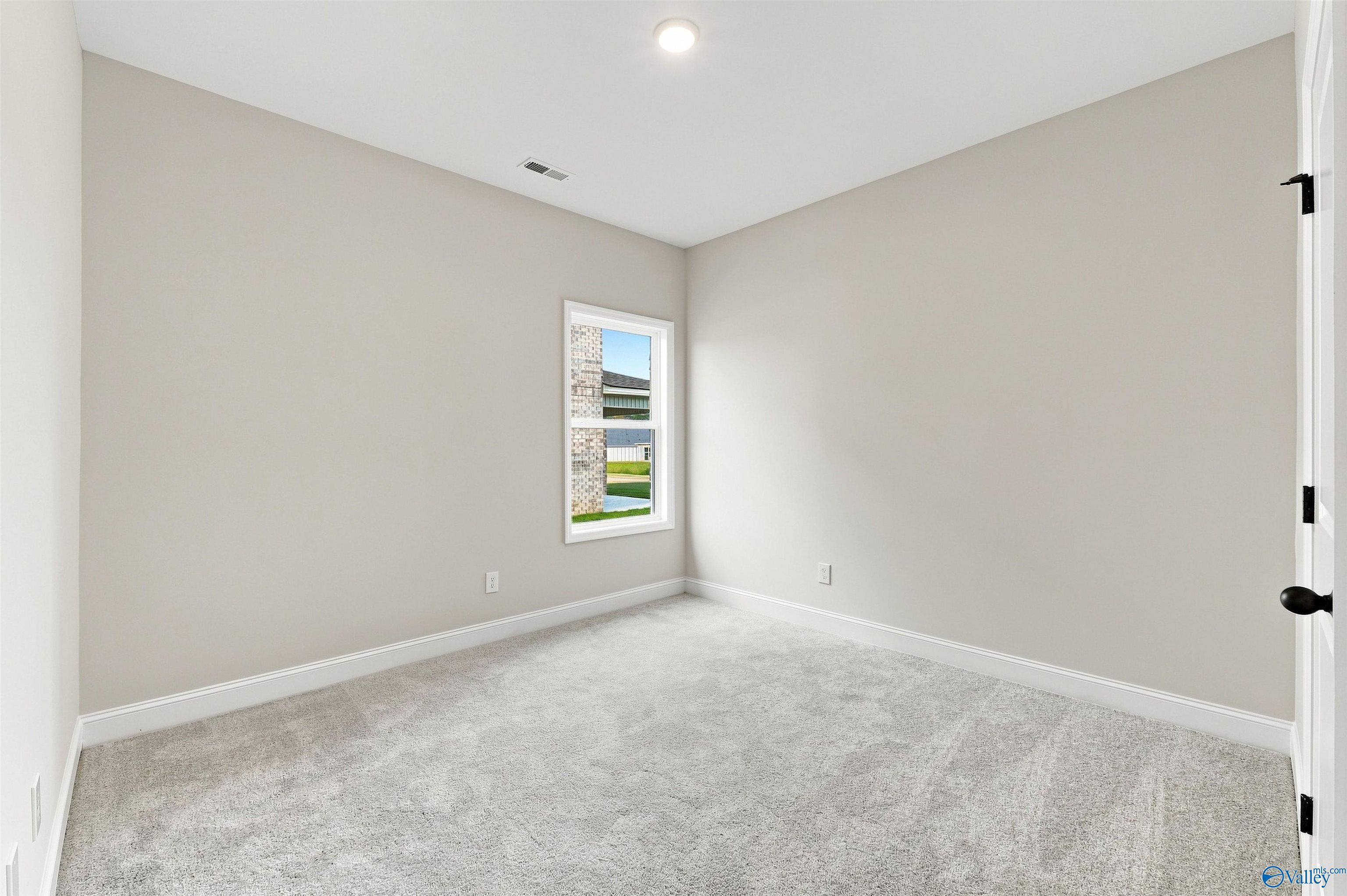 Bright empty bedroom with plush gray carpet, neutral walls, and window view in Davidson Homes Franklin C plan, The Meadows, Athens, AL