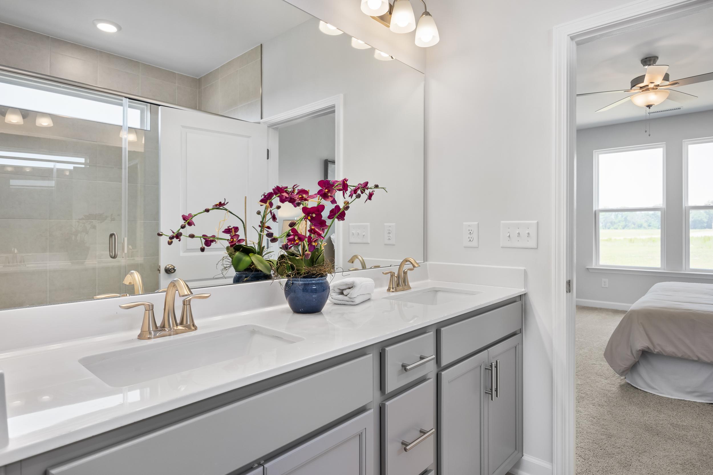 Modern master bathroom in The Daphne D featuring double gray vanity, orchids, glass shower, and bedroom view