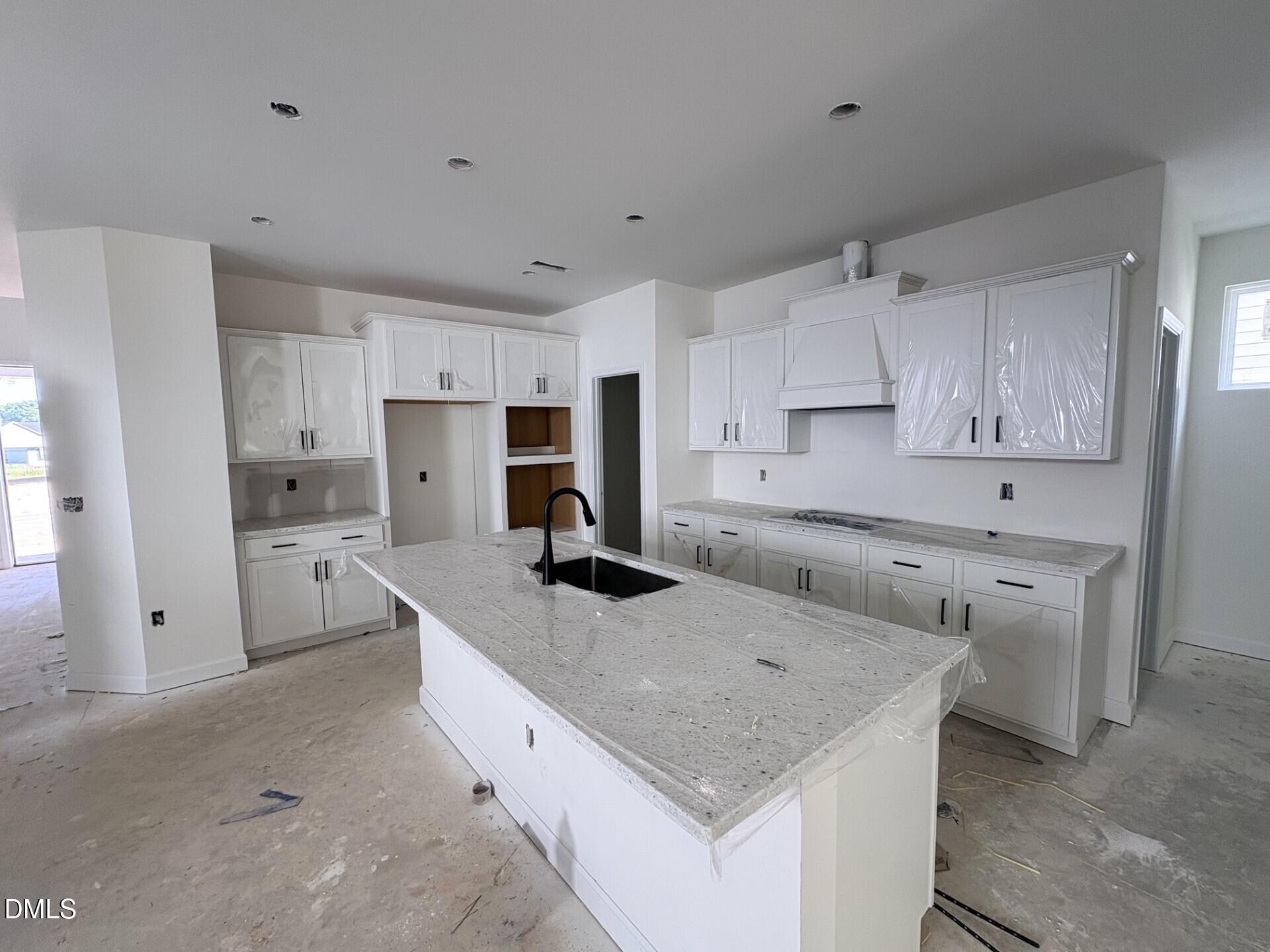 White shaker kitchen with large granite island and black faucet in Davidson Homes The Adalynn A, Woodland Crossing, Zebulon NC