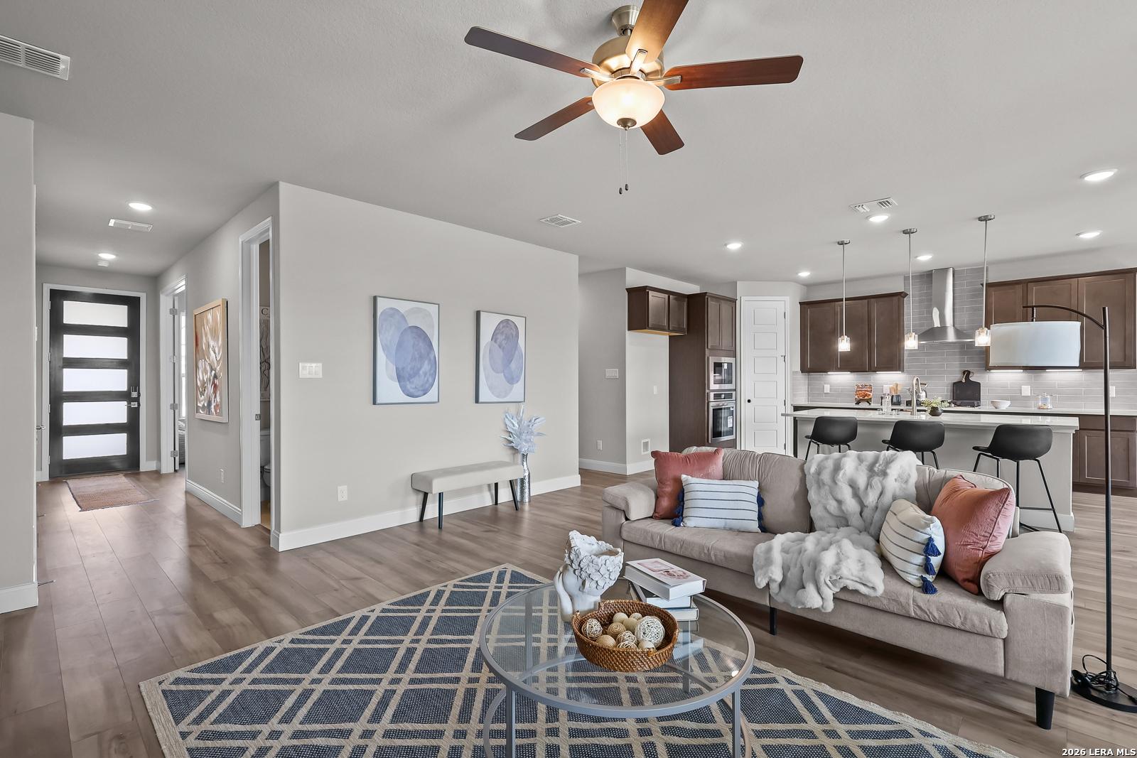 Open-concept living room with plush sofa, abstract wall art, and adjacent kitchen island in Davidson Homes The Rockford G, Ladera, San Antonio