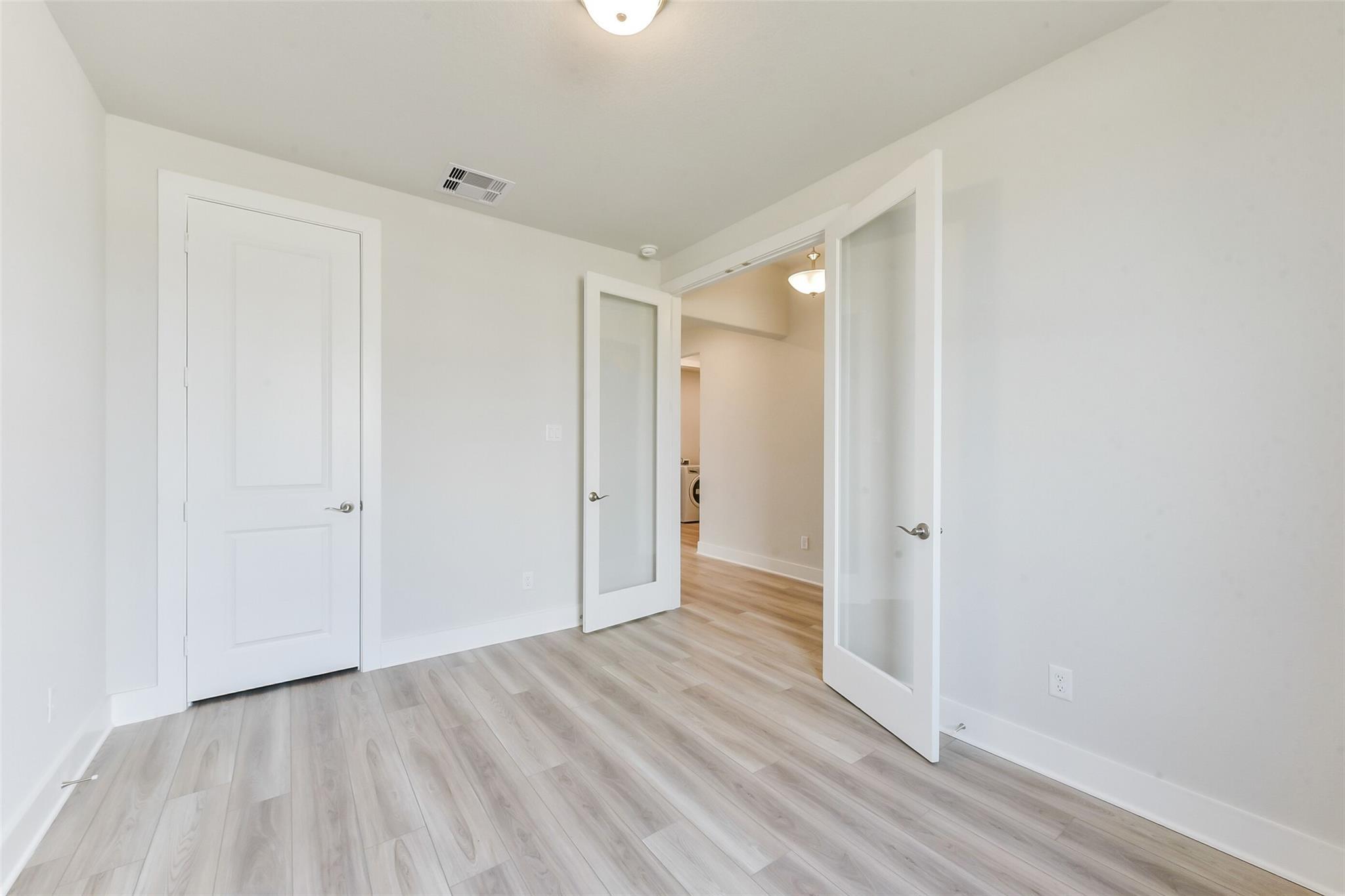 Bright bedroom with open French doors, white walls, and light oak flooring in Davidson Homes The Edward A, Texas City