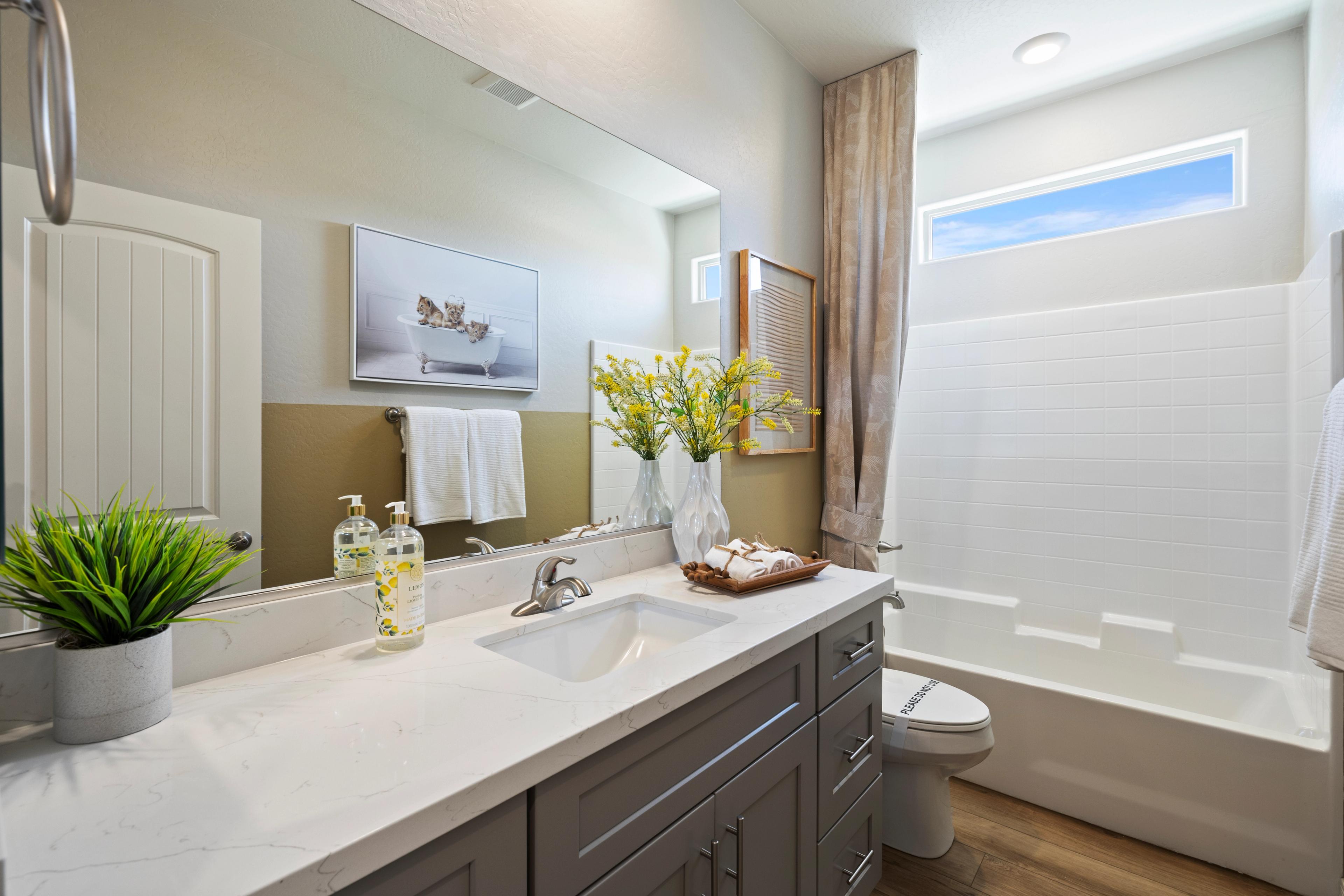 Spacious bathroom at North Ridge Pronghorn Ranch in Prescott Valley AZ with quartz double vanity, gray cabinets, white tile shower, tub, yellow flowers