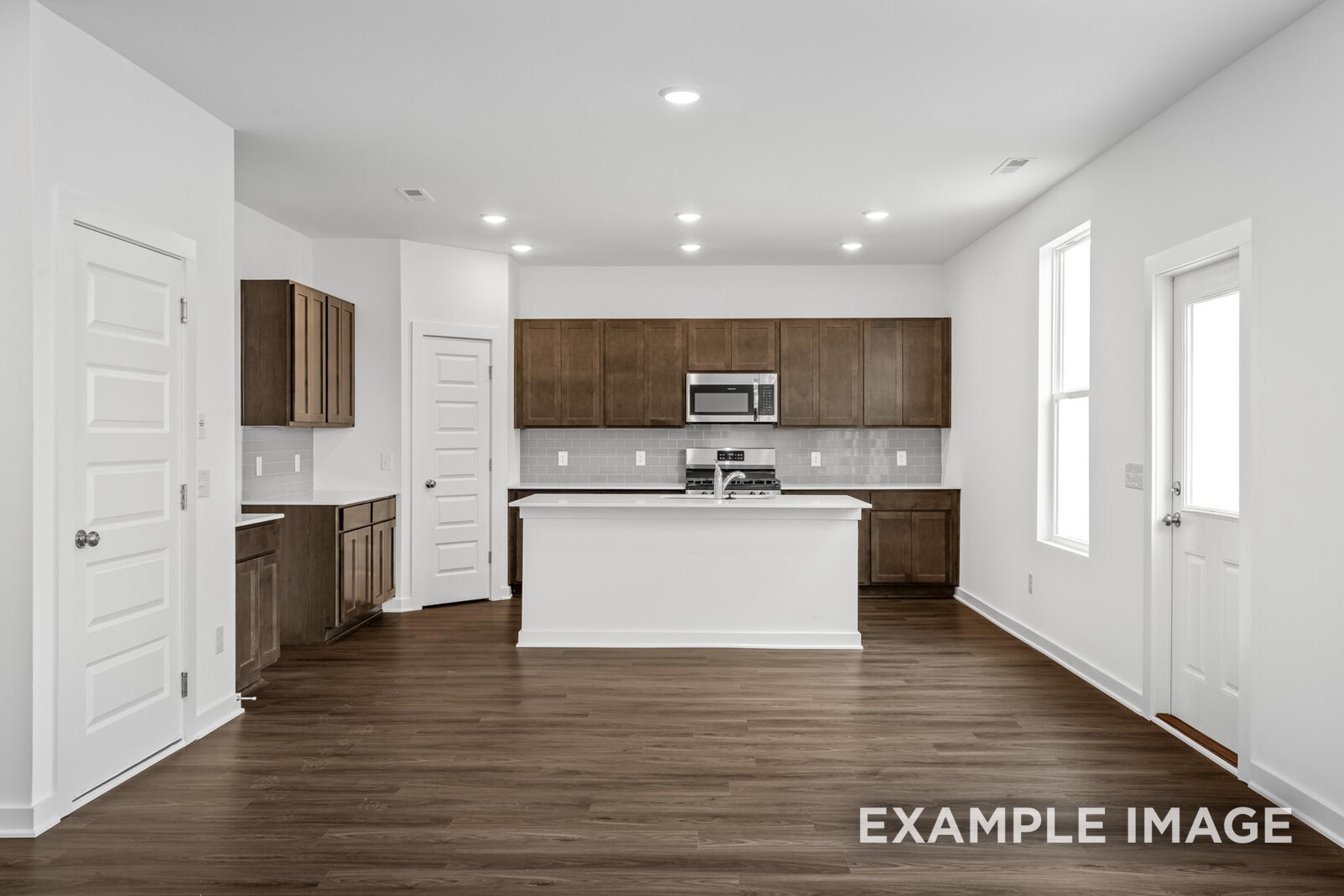 Spacious modern kitchen in The Logan C home design by Davidson Homes featuring white island, shaker cabinets, stainless appliances, hardwood floors