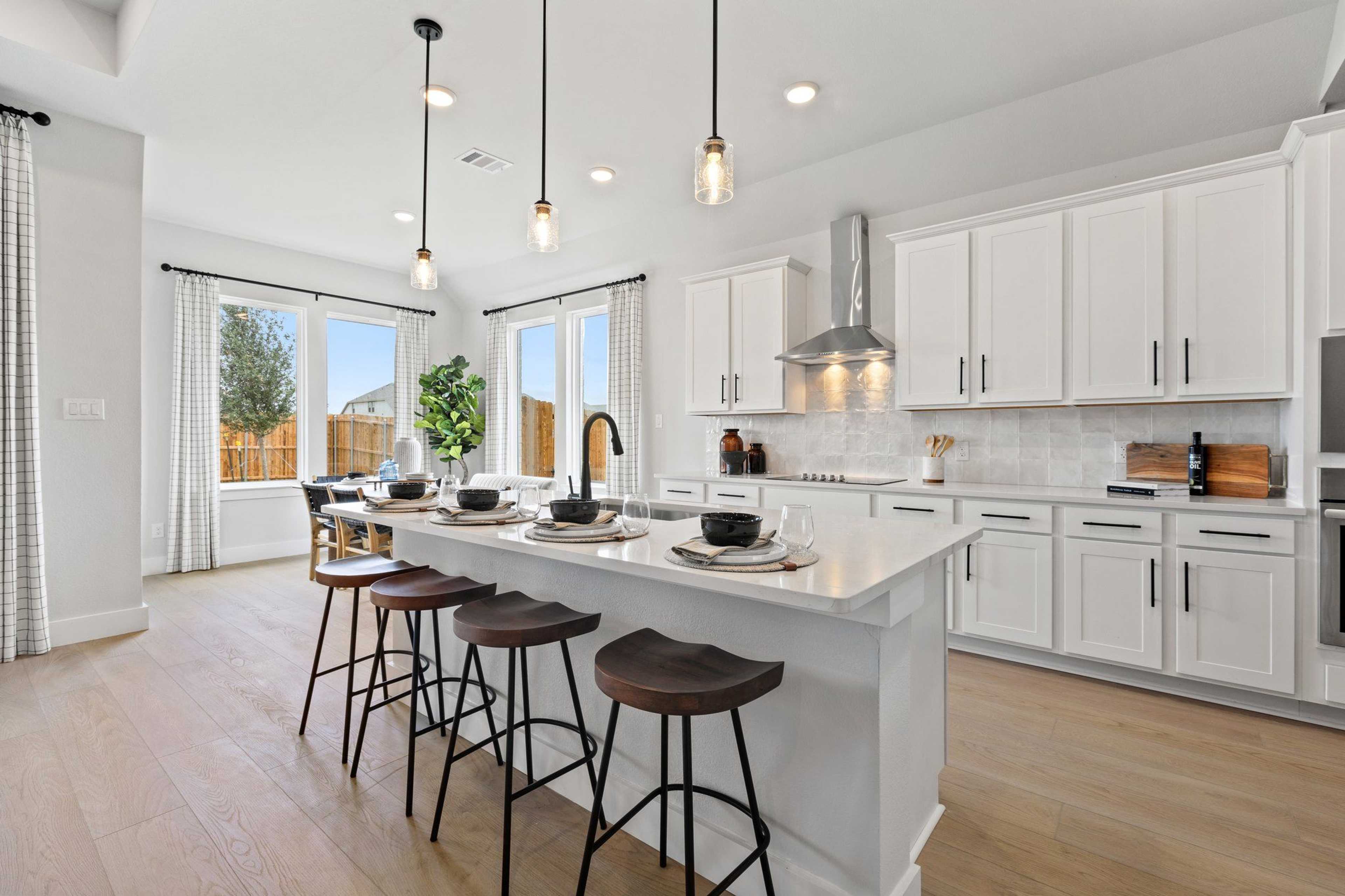 Modern white kitchen with large island, bar stools, pendant lights, and large windows at Parks at Foster Crossing, Anna TX