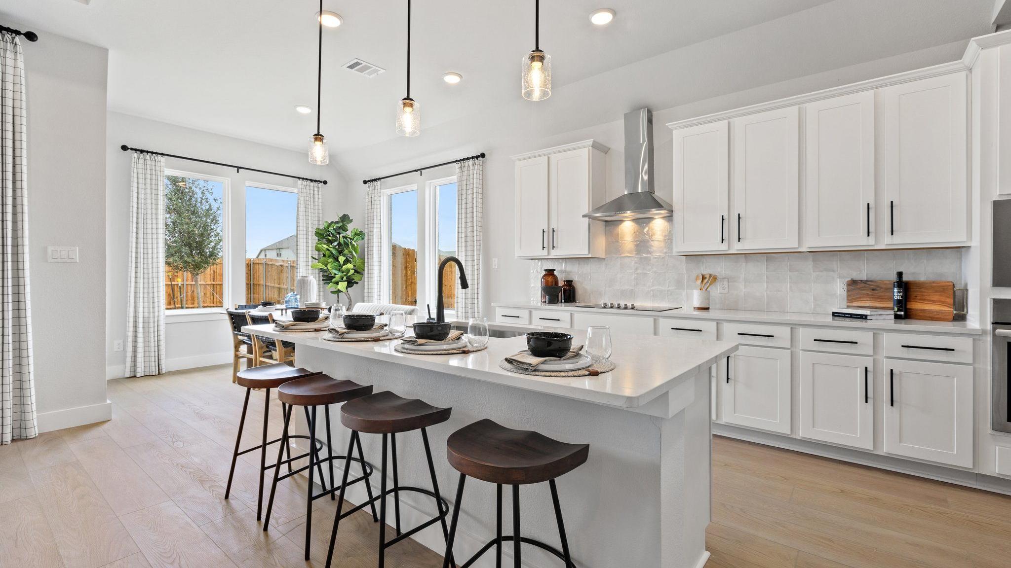 Modern white kitchen with large island, bar stools, pendant lights, and large windows at Parks at Foster Crossing, Anna TX