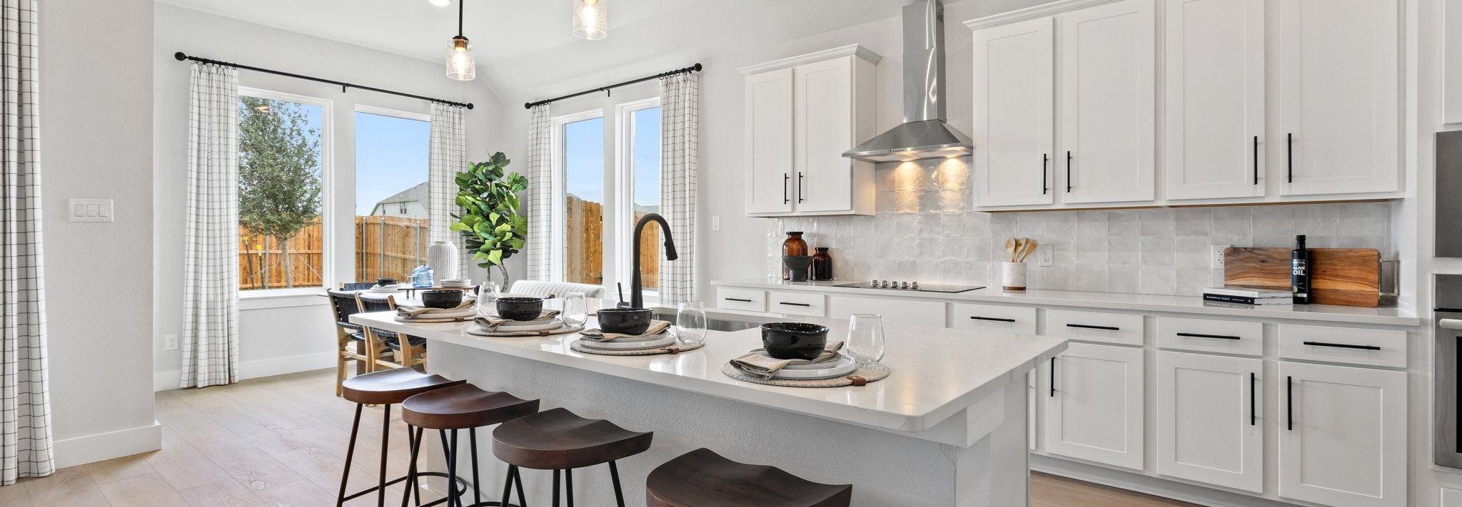 Modern white kitchen with large island, bar stools, pendant lights, and large windows at Parks at Foster Crossing, Anna TX