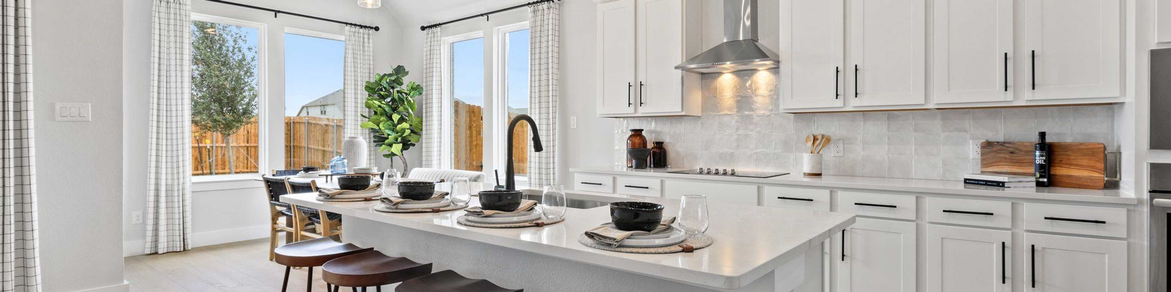 Modern white kitchen with large island, bar stools, pendant lights, and large windows at Parks at Foster Crossing, Anna TX