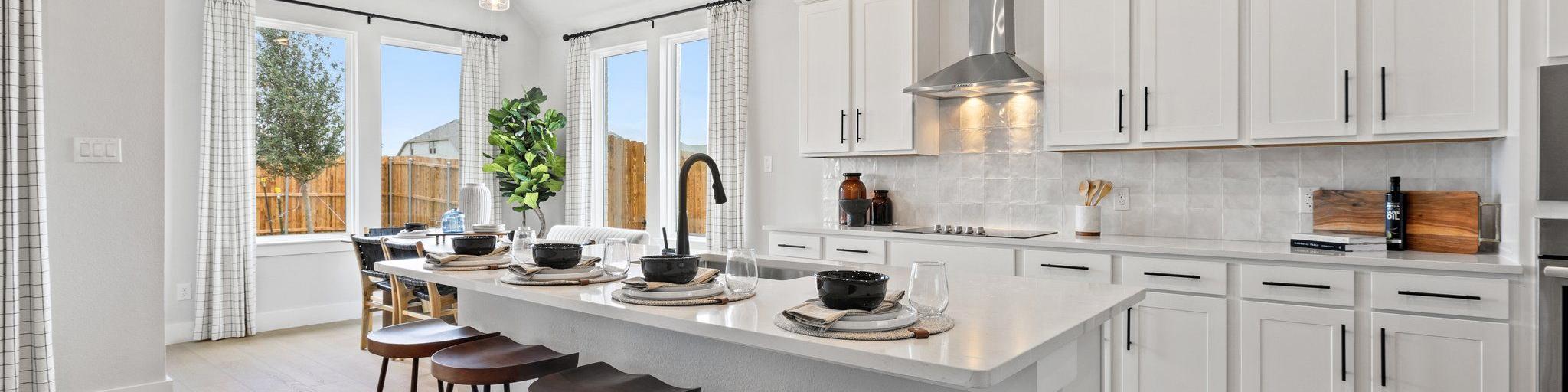 Modern white kitchen with large island, bar stools, pendant lights, and large windows at Parks at Foster Crossing, Anna TX