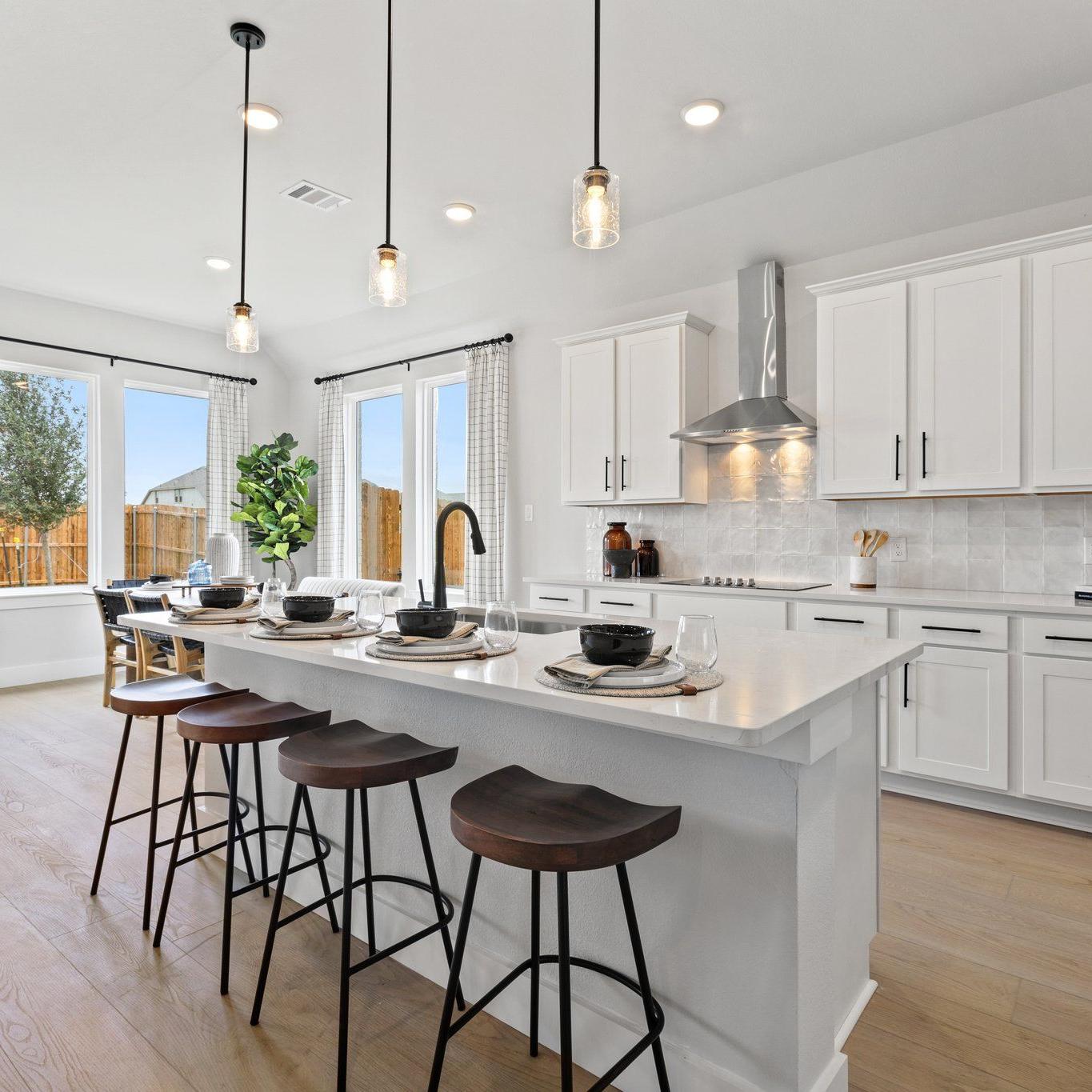 Modern white kitchen with large island, bar stools, pendant lights, and large windows at Parks at Foster Crossing, Anna TX