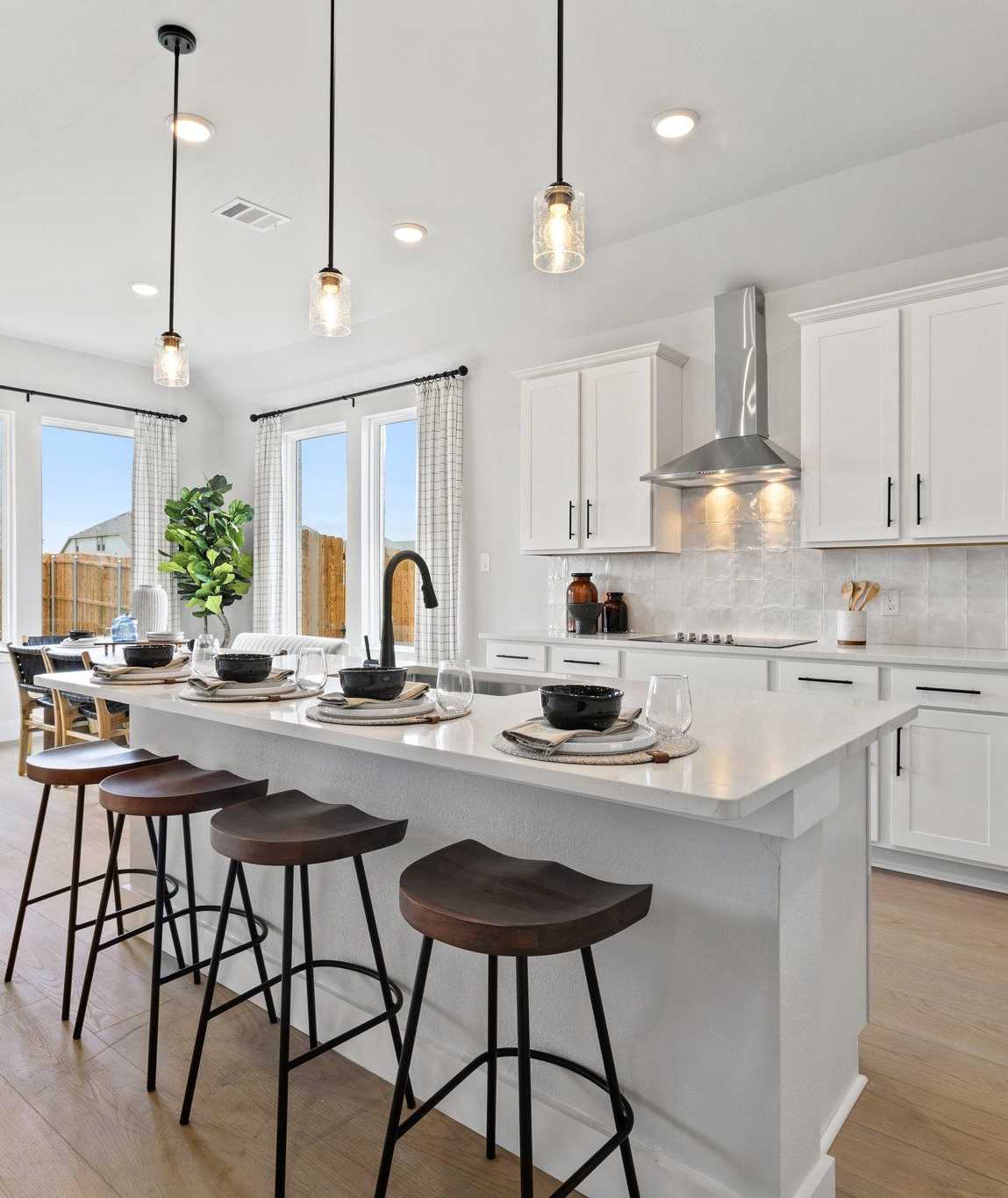 Modern white kitchen with large island, bar stools, pendant lights, and large windows at Parks at Foster Crossing, Anna TX