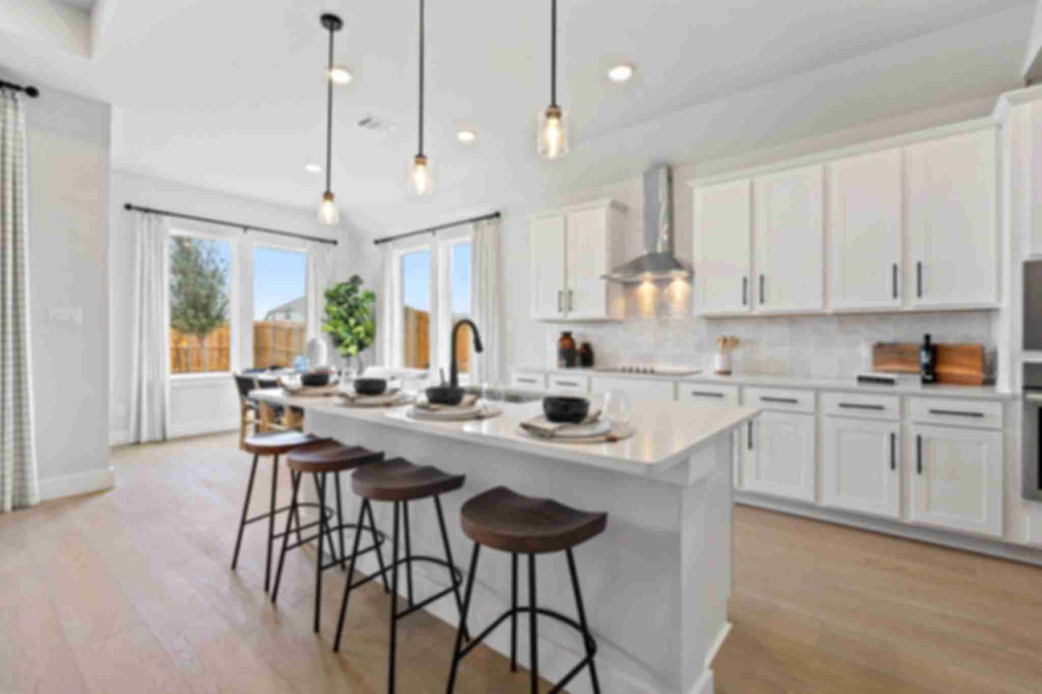 Modern white kitchen with large island, bar stools, pendant lights, and large windows at Parks at Foster Crossing, Anna TX