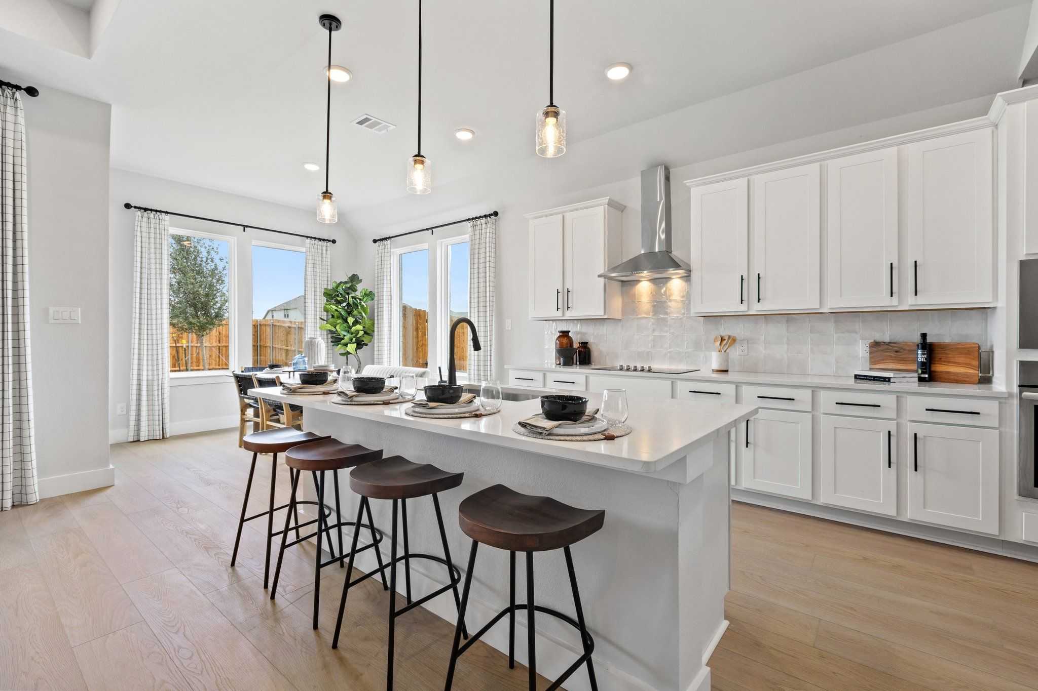 Modern white kitchen with large island, bar stools, pendant lights, and large windows at Parks at Foster Crossing, Anna TX