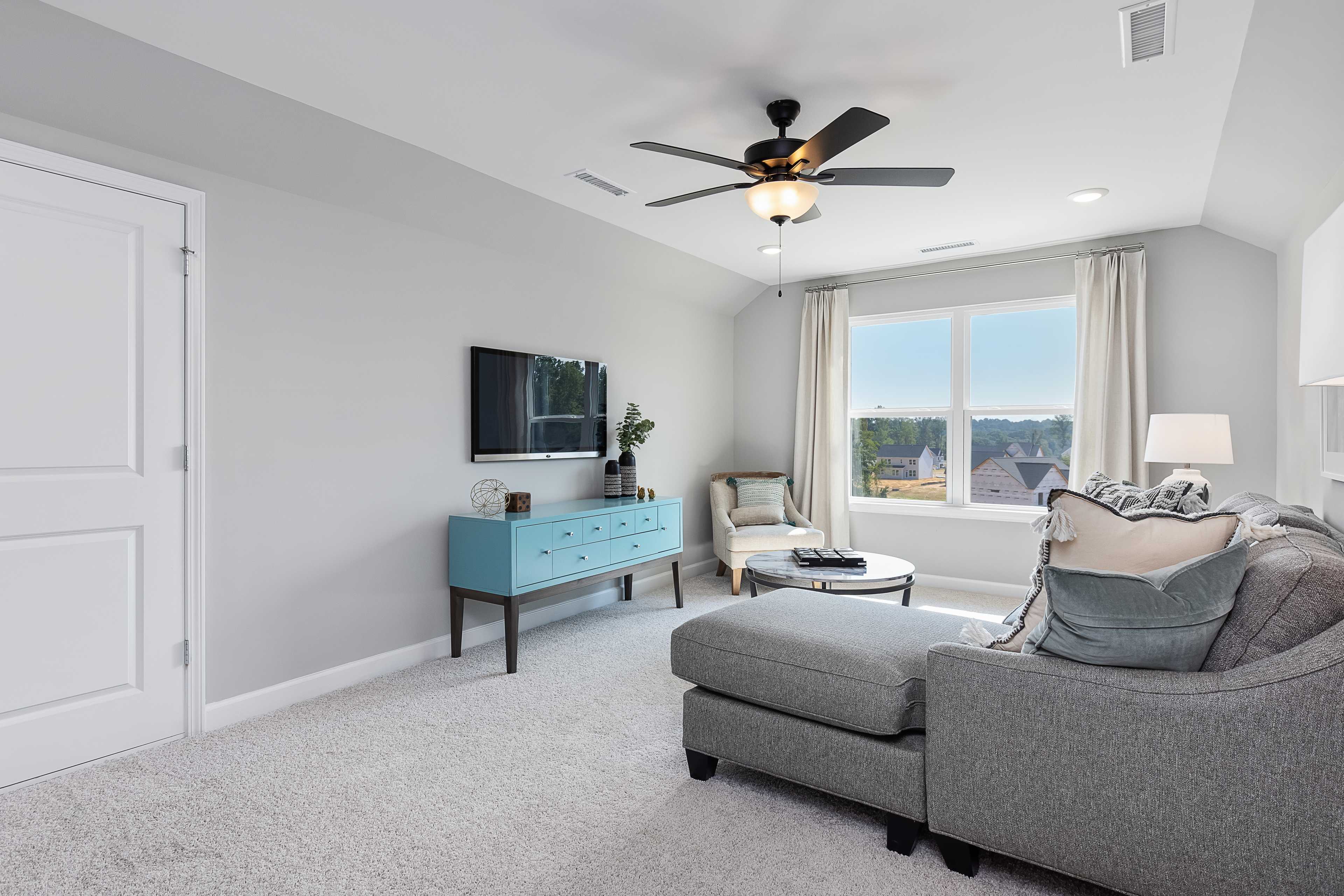 Cozy loft room at Enclave at Belmont in Belmont NC with gray sectional sofa, armchair, mounted TV, and large window view