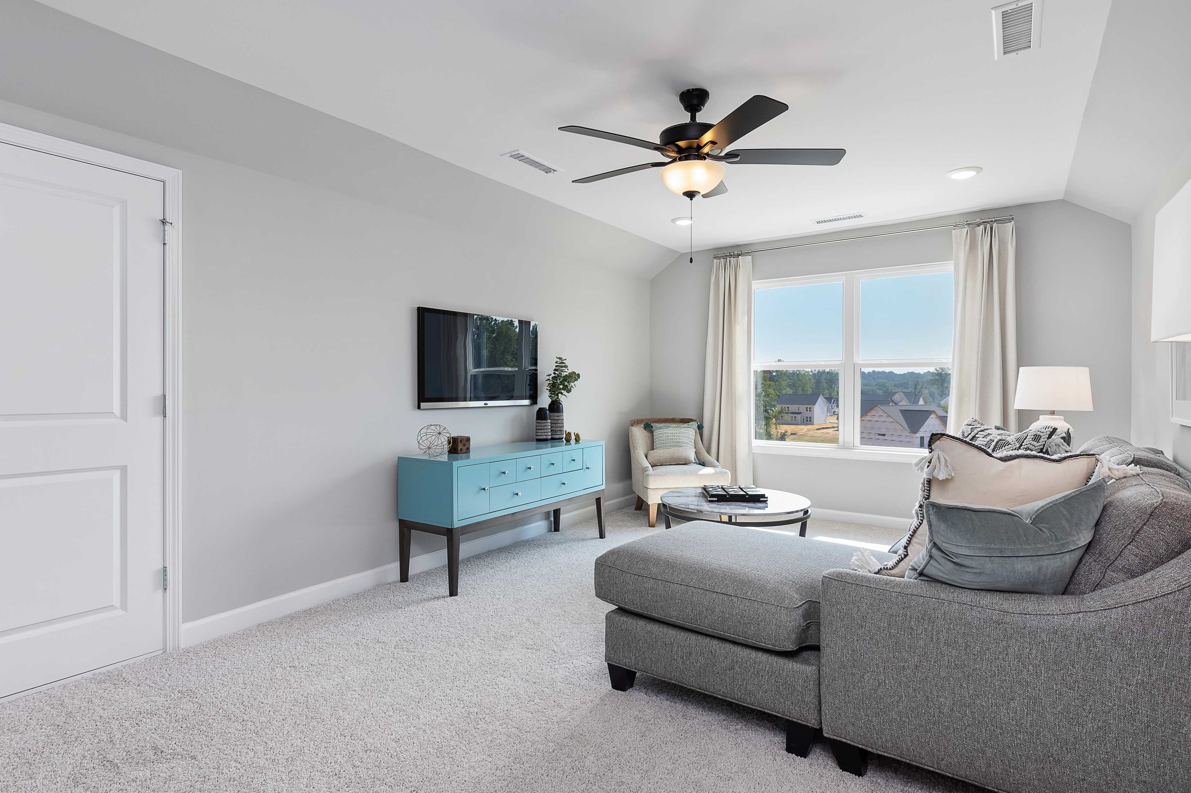 Cozy loft room at Enclave at Belmont in Belmont NC with gray sectional sofa, armchair, mounted TV, and large window view