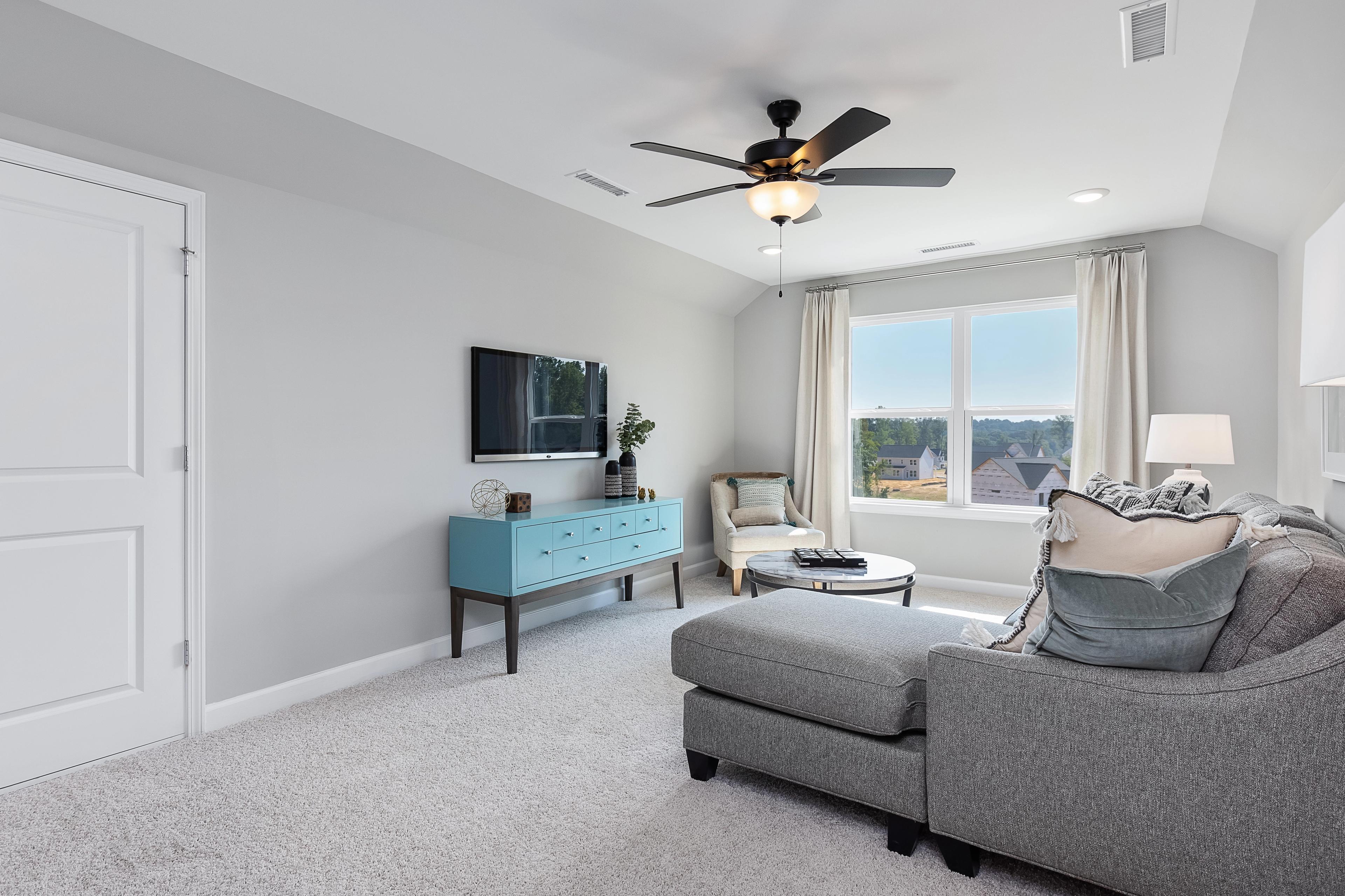 Cozy loft room at Enclave at Belmont in Belmont NC with gray sectional sofa, armchair, mounted TV, and large window view