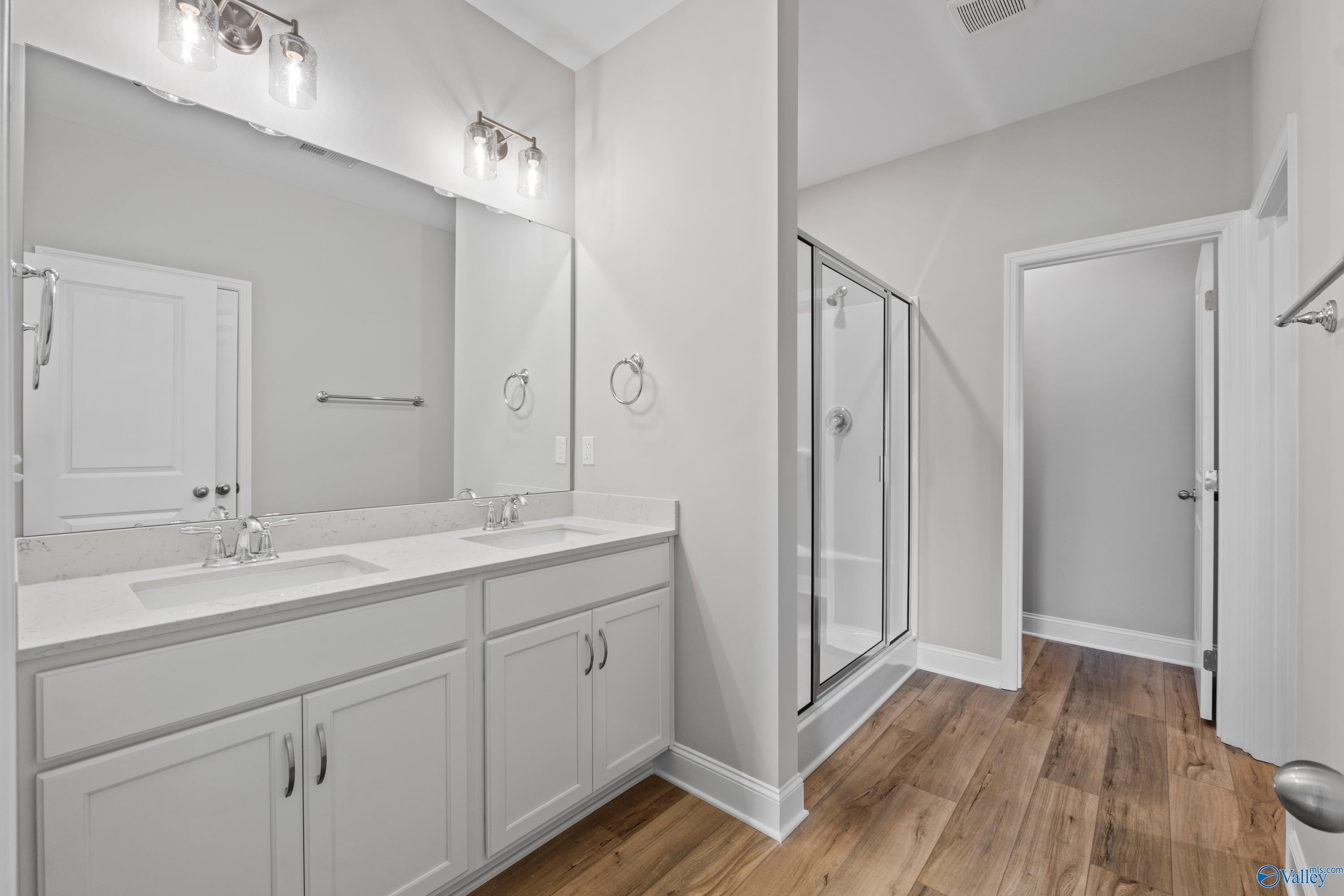 Modern master bathroom featuring double white vanity, frameless glass shower, and hardwood floors in Davidson Homes The Daphne C, Athens, AL