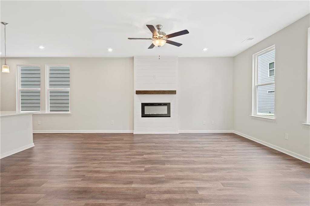 Cozy living room featuring white brick fireplace, hardwood floors, and ceiling fan in Davidson Homes The Cary B, Kennesaw, Georgia